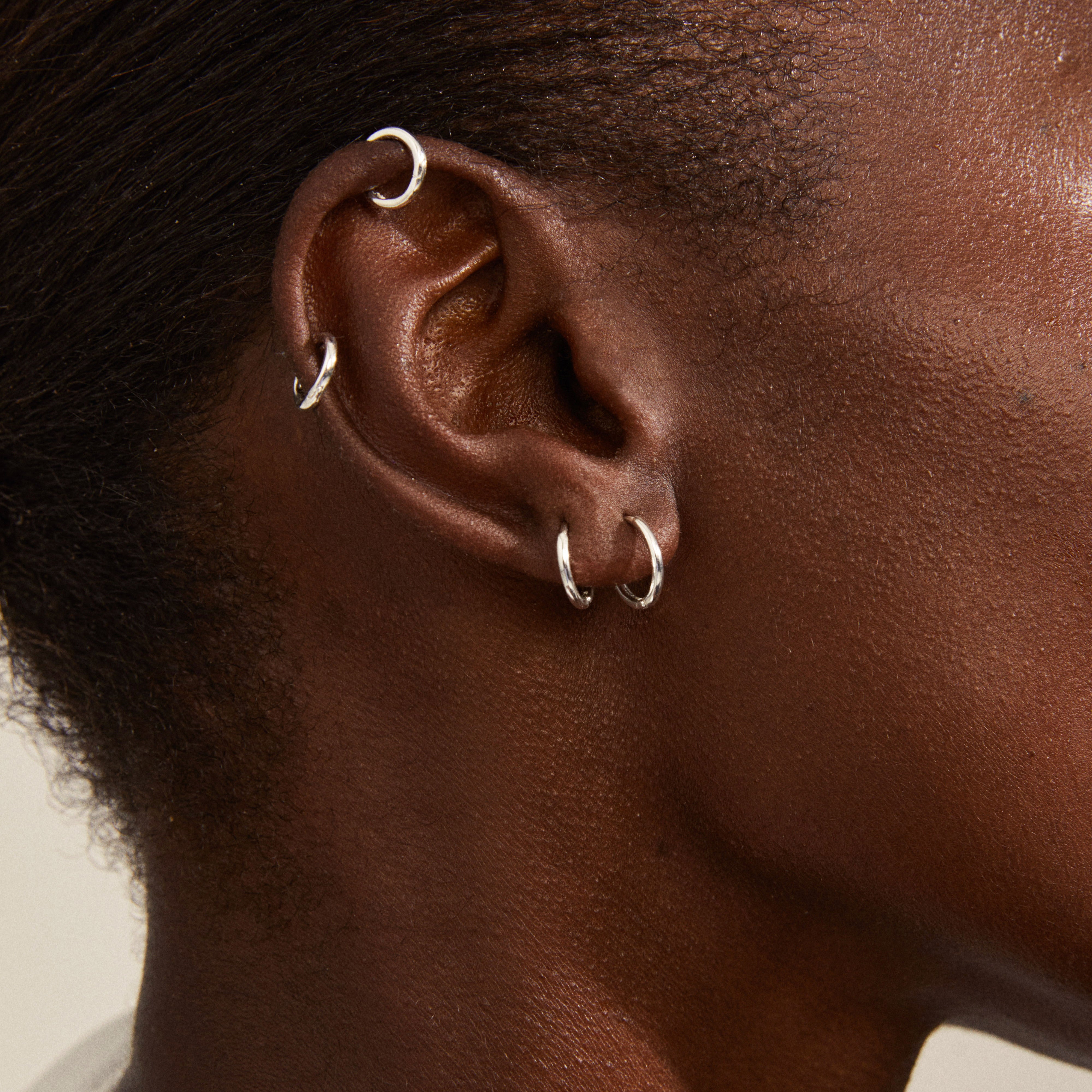 Close-up of an ear adorned with the LEAF 2-in-1 set huggie hoops, showcasing four silver-plated, recycled mini hoops by Pilgrim, emphasizing classic style.