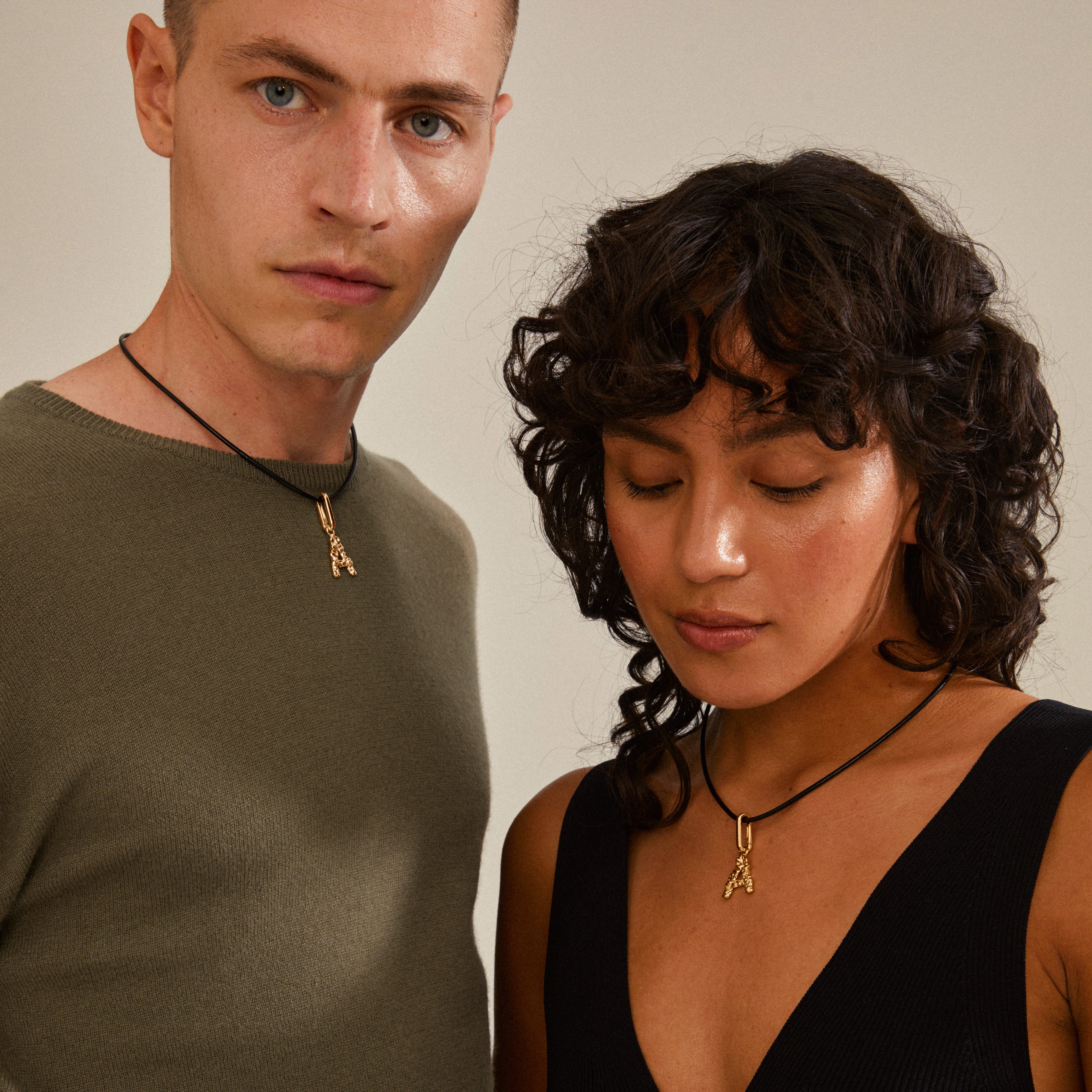 Gold-plated CHARM pendant A from Pilgrim, worn on a necklace by a woman with curly hair, showcasing a personalized and stylish accessory.