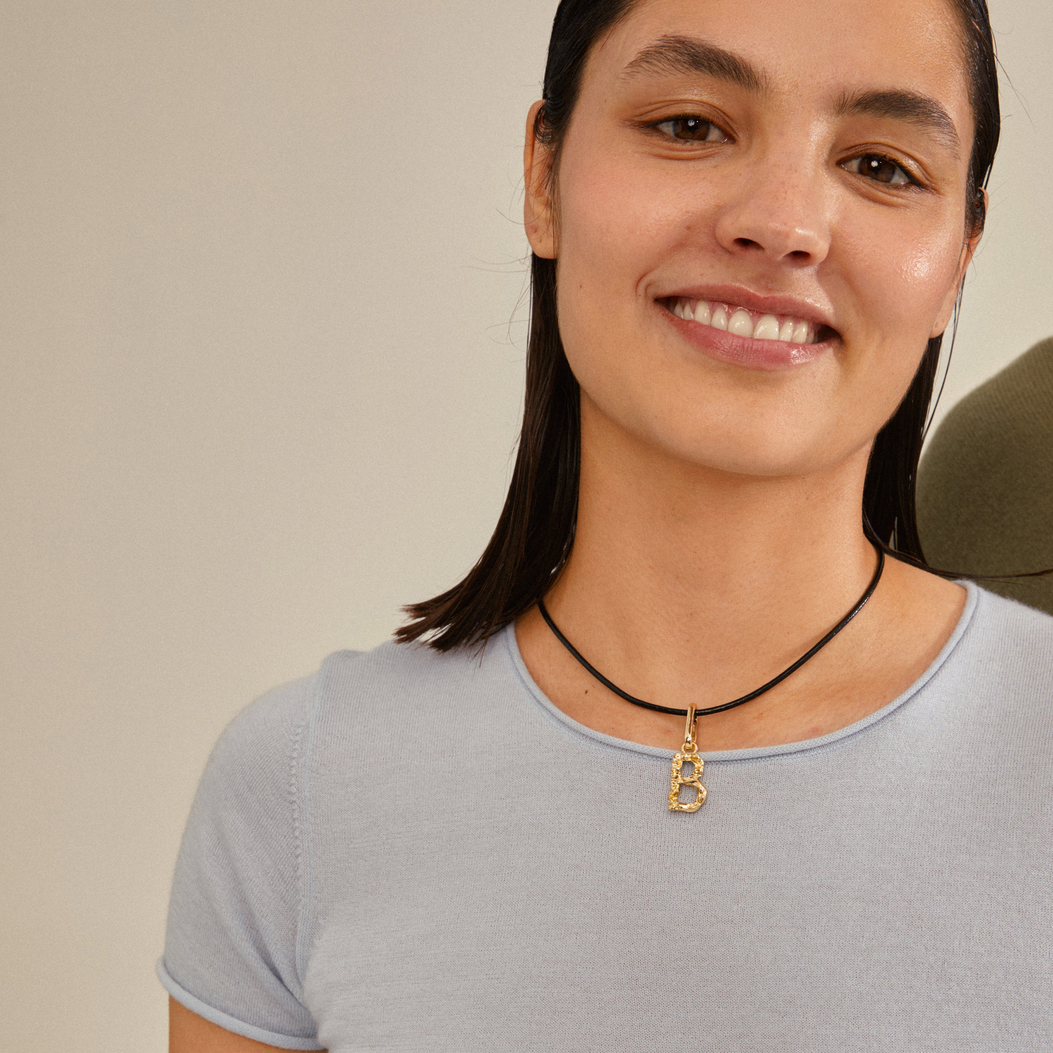 Woman wearing a gold-plated CHARM pendant B necklace, smiling. The pendant hangs on a chain, offering a personalized, stylish look with recycled materials.