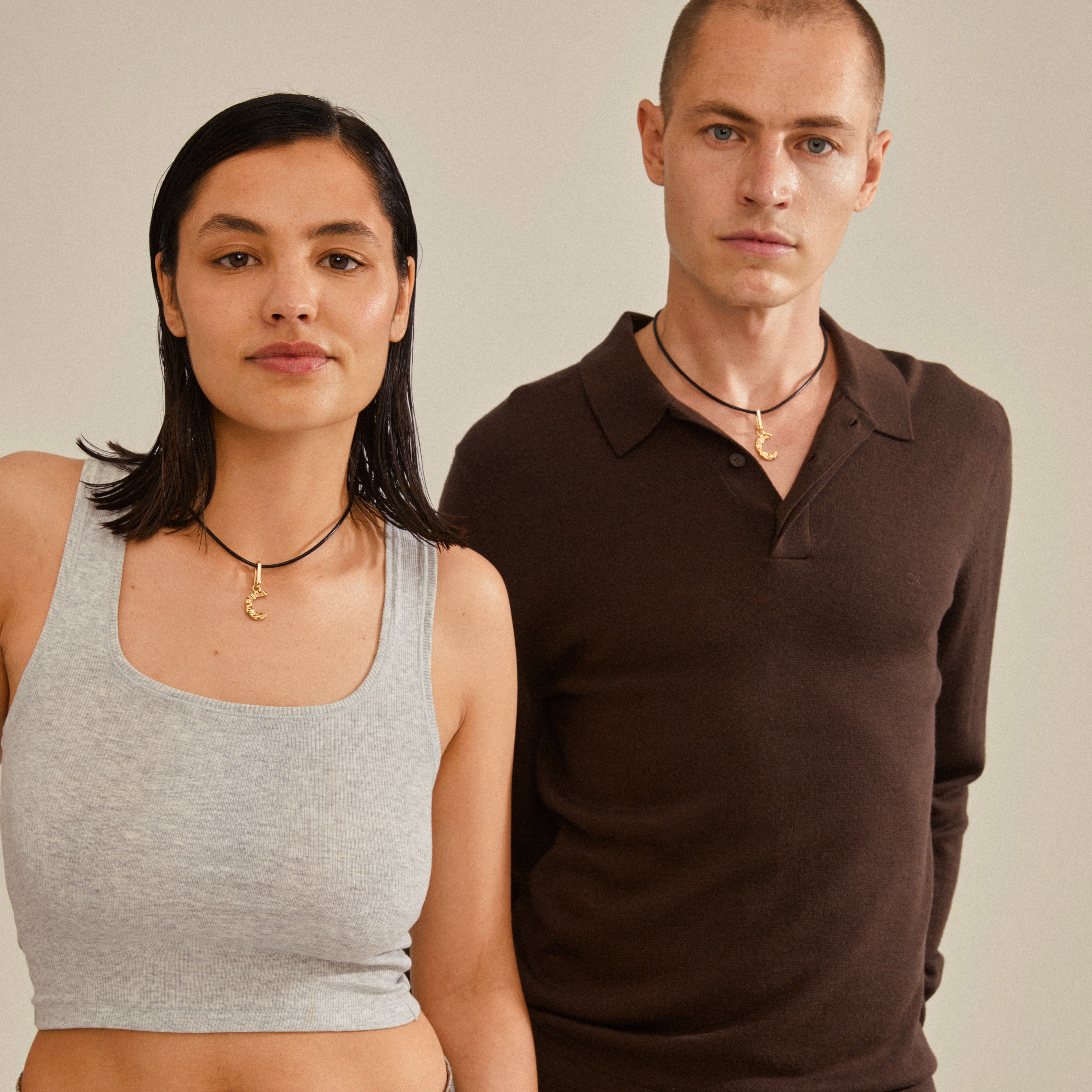 A man and woman showcase Pilgrim's CHARM pendant C, gold-plated, highlighting its personalized style and eco-friendly design.