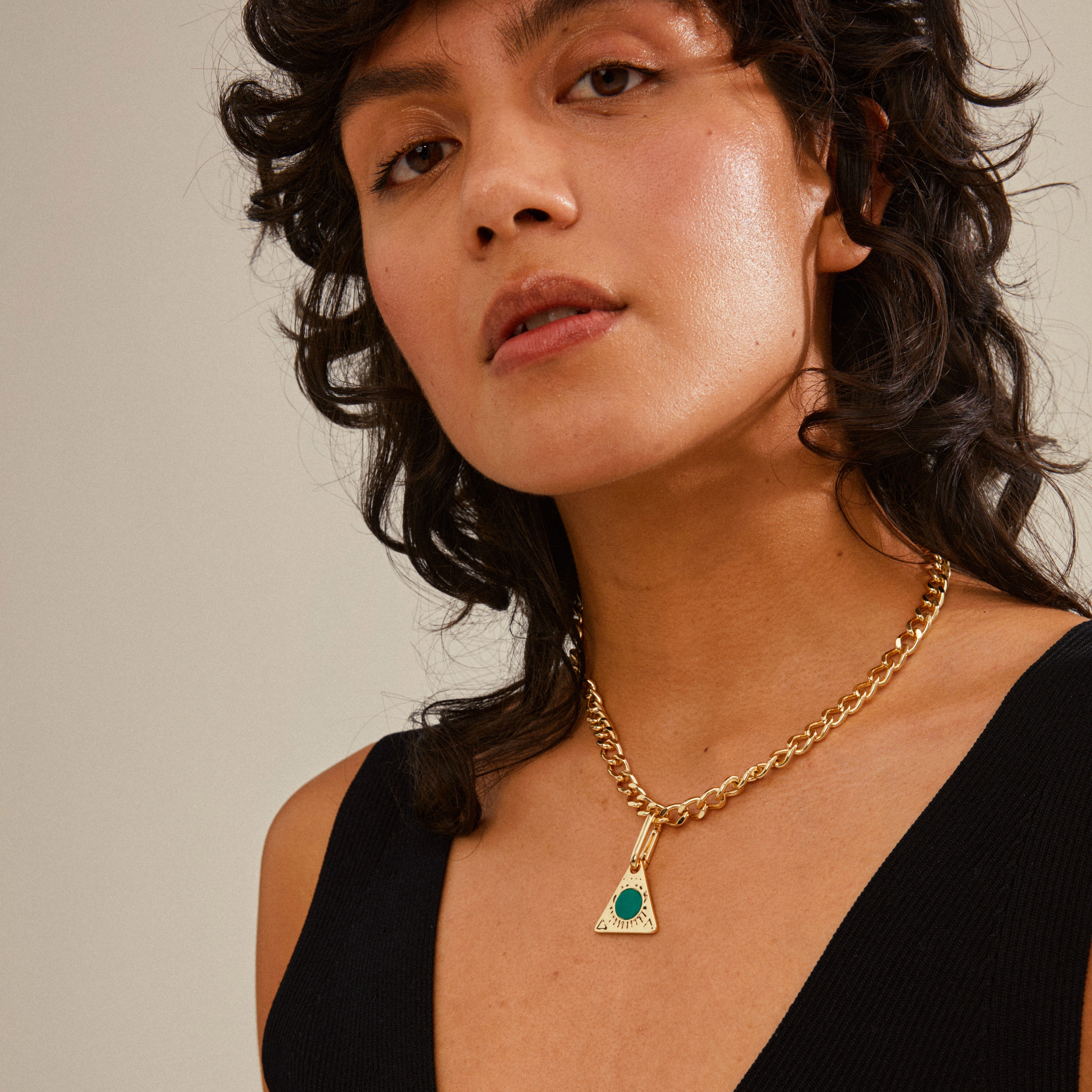 Woman wearing a Pilgrim CHARM triangle pendant, green/gold-plated, highlighting its intricate design and personalized styling options for a unique fashion statement.