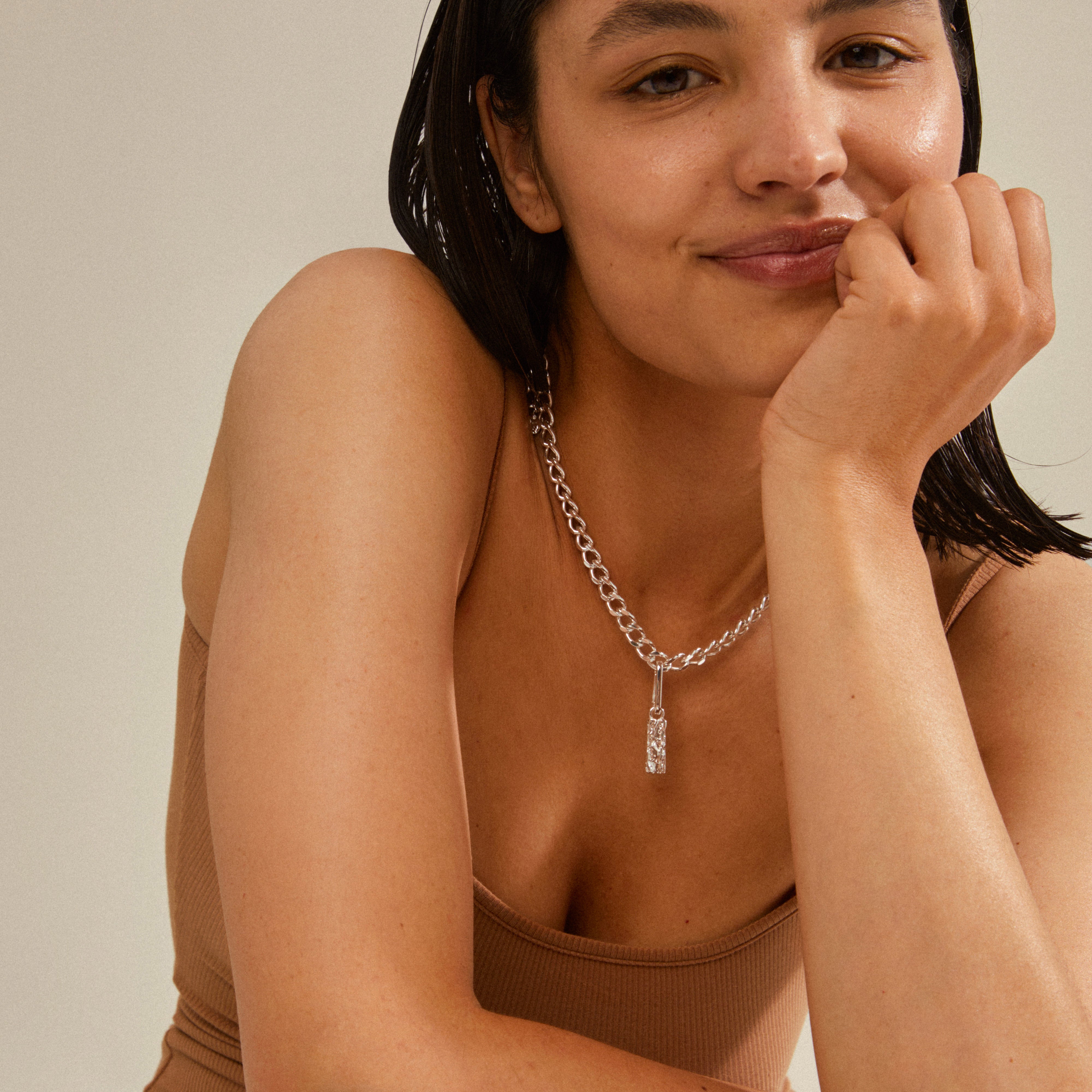 Woman smiling, wearing Pilgrim's CHARM tag pendant, a silver-plated accessory, showcasing a personalized and eco-friendly style statement.