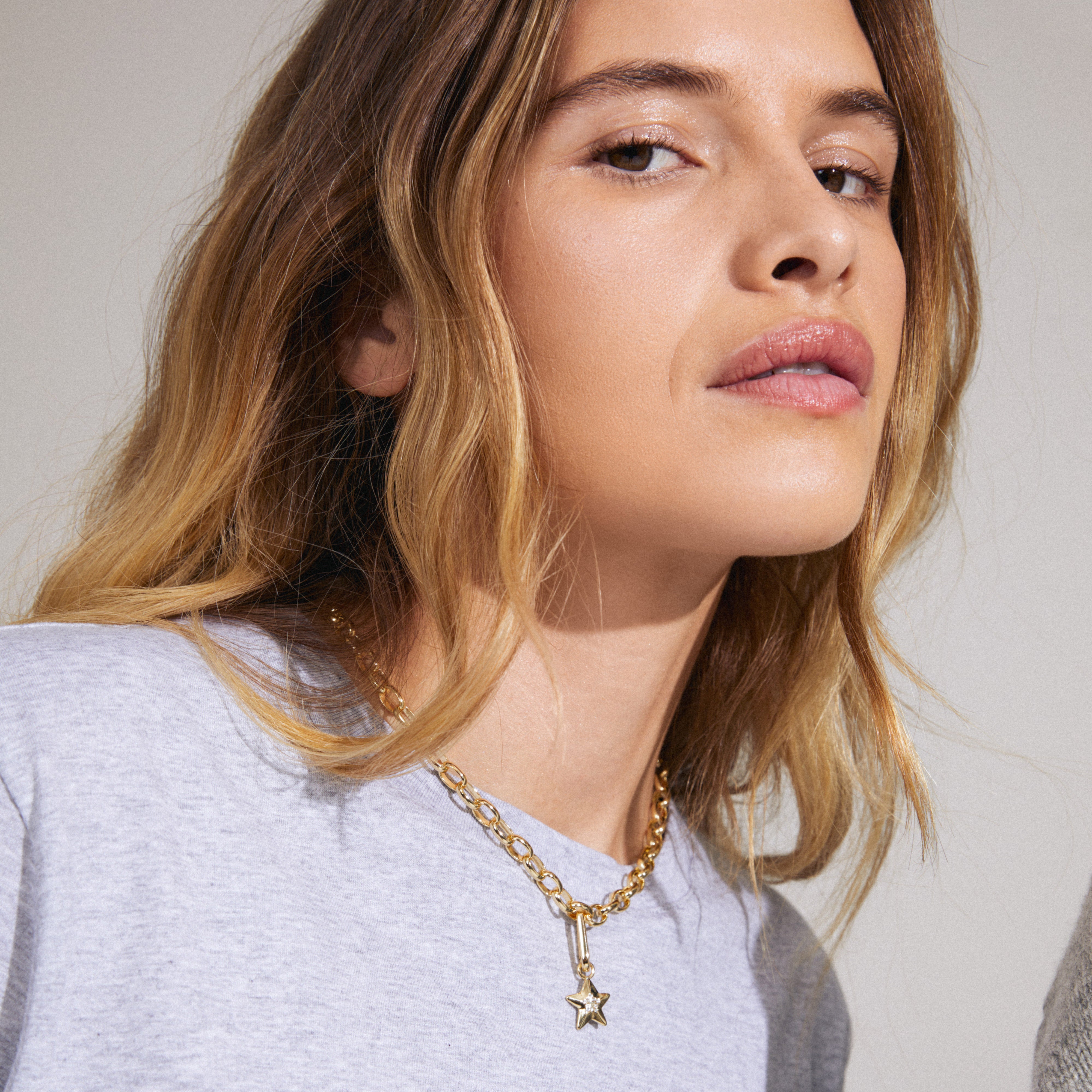 A woman wearing a gold-plated CHARM star pendant necklace with Preciosa crystals, highlighting Pilgrim's blend of timeless and trendy Danish jewelry design.