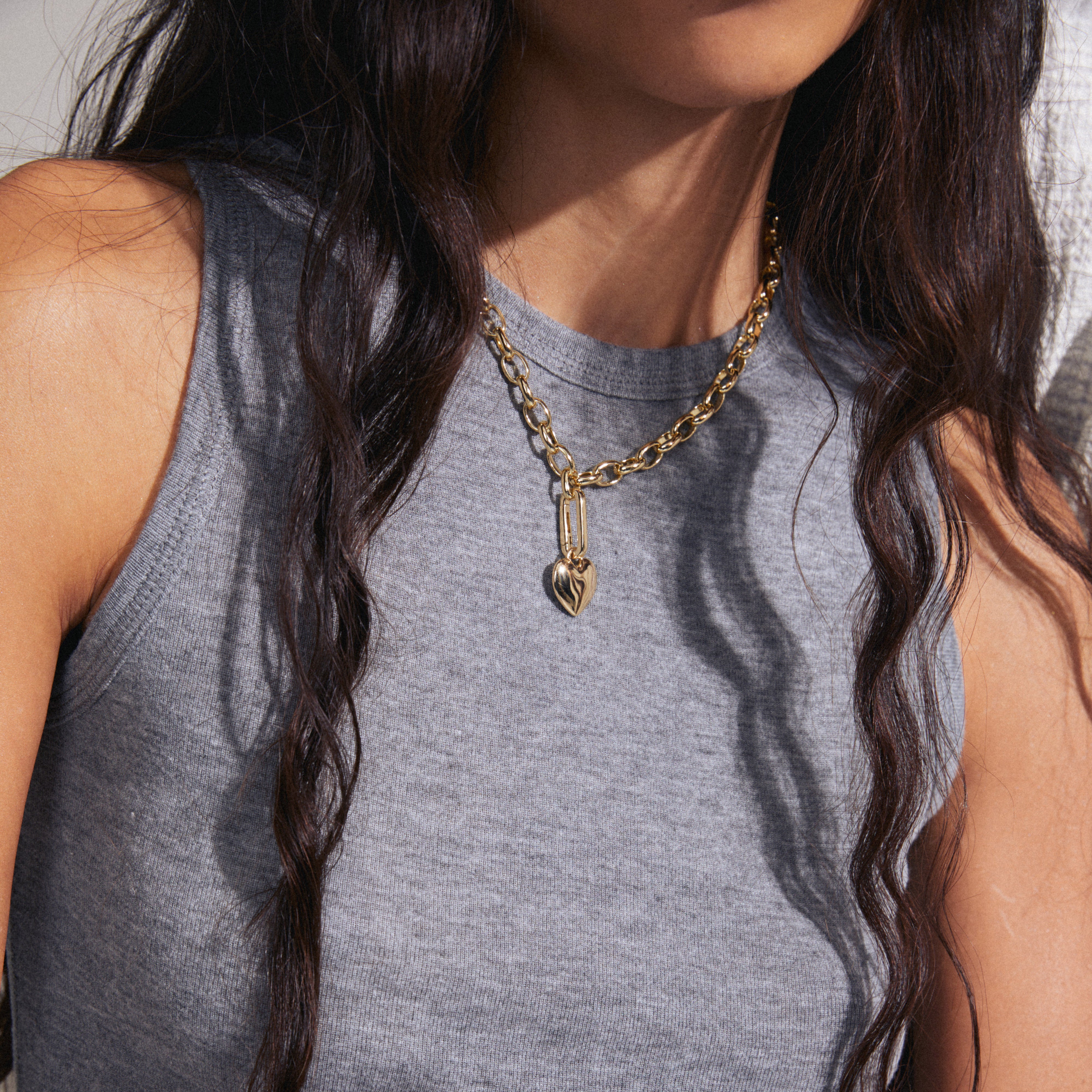 Woman wearing Pilgrim's CHARM heart pendant, gold-plated, highlighting its shiny, recycled design on a necklace, perfect for personalized and stylish accessorizing.