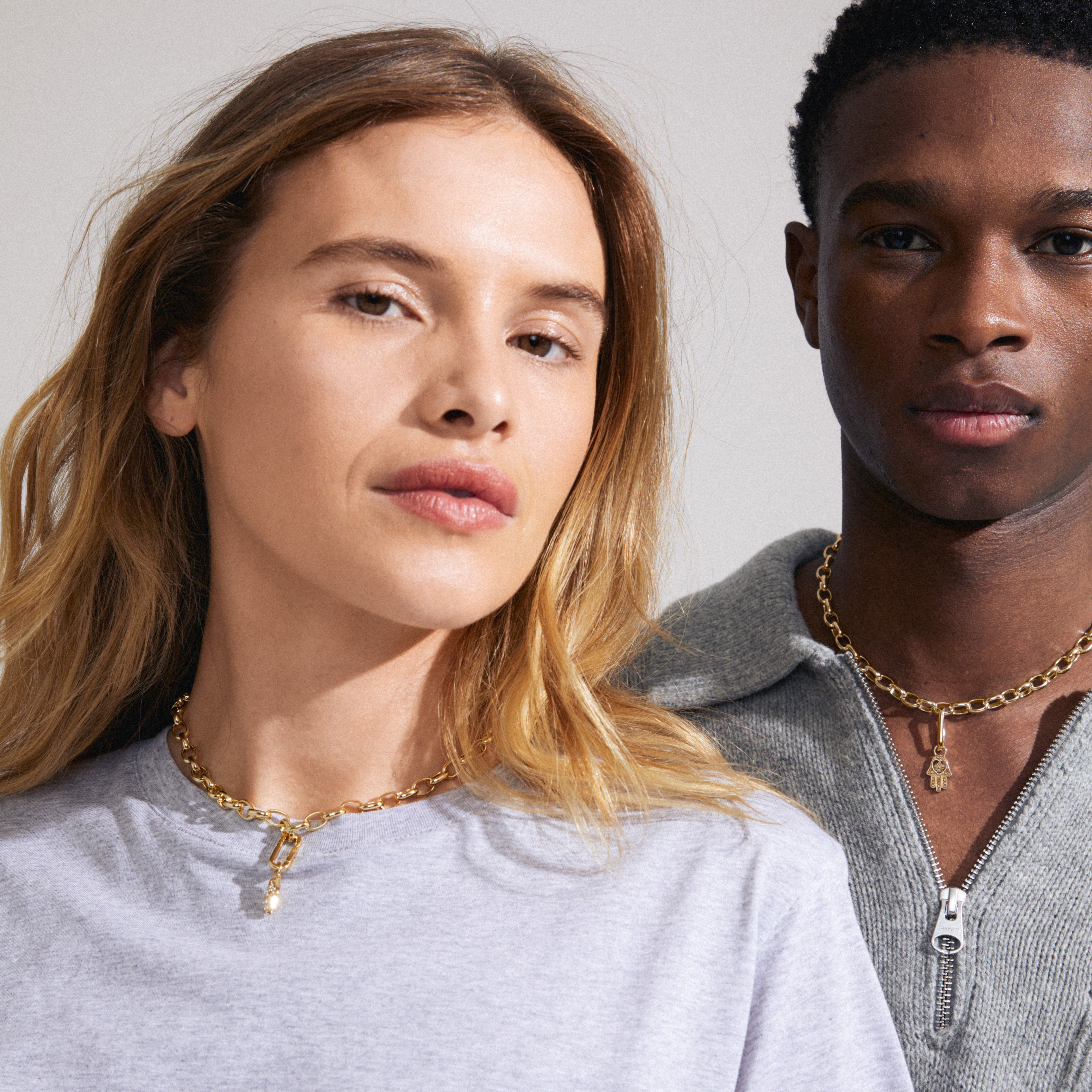 Man and woman showcasing Pilgrim's CHARM Hamsa pendant, gold-plated with Preciosa crystals, worn as a fashion statement piece.