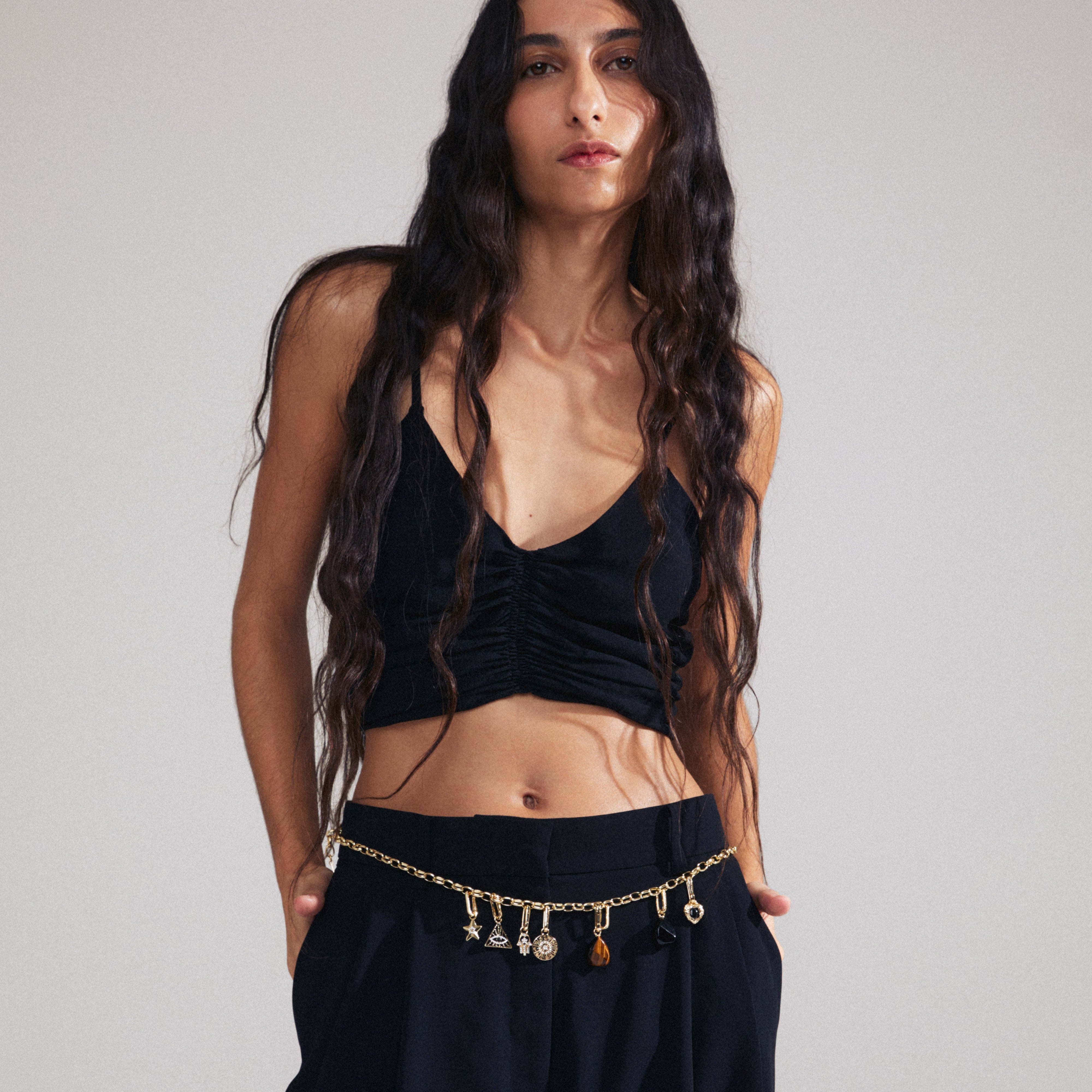 Woman showcases Pilgrim's CHARM triangle pendant, gold-plated with all-seeing eye, styled with black outfit, emphasizing unique, personalized fashion statement.