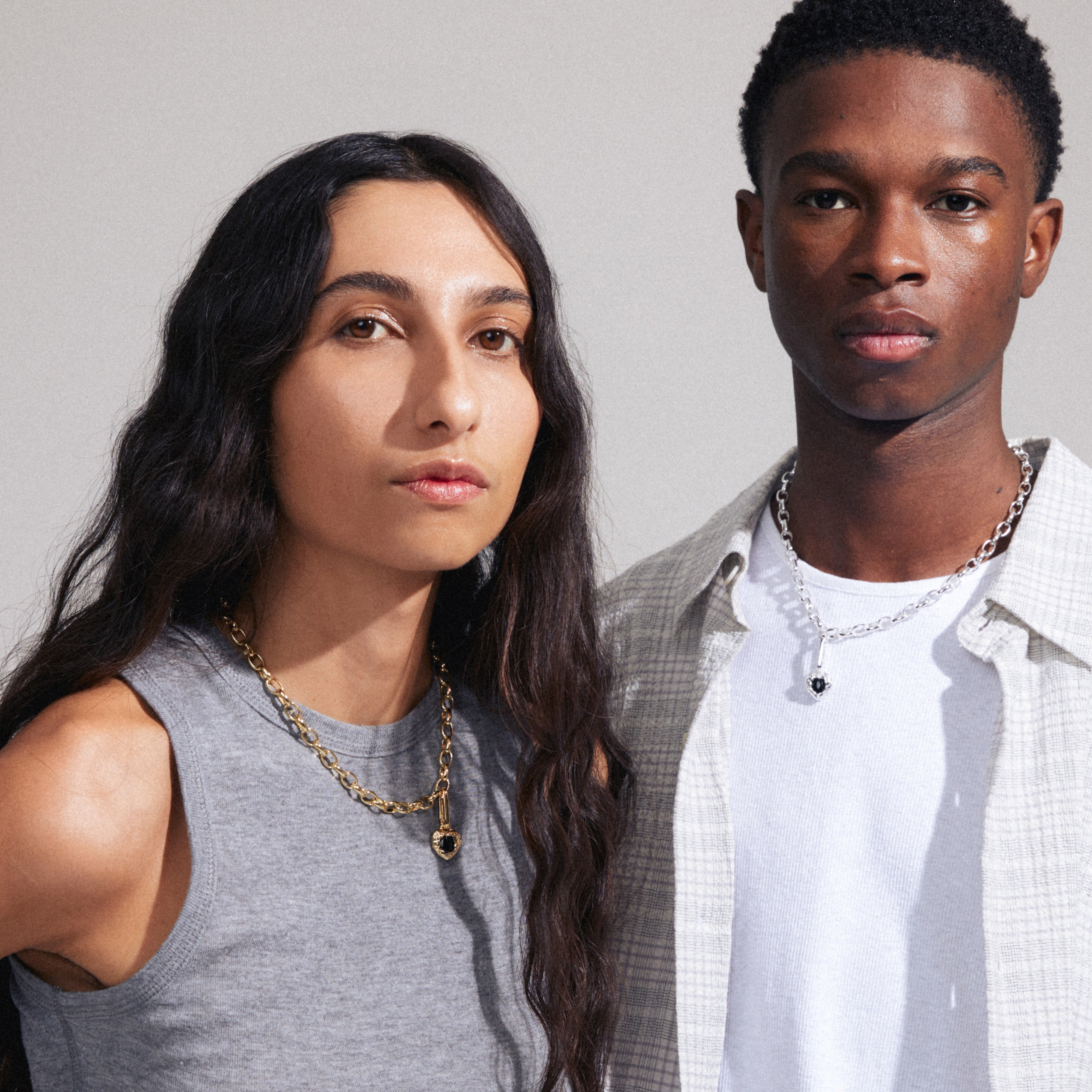 A man and woman wearing Pilgrim's CHARM black agate pendant, gold-plated, showcasing its elegant design and versatility on different necklace styles.