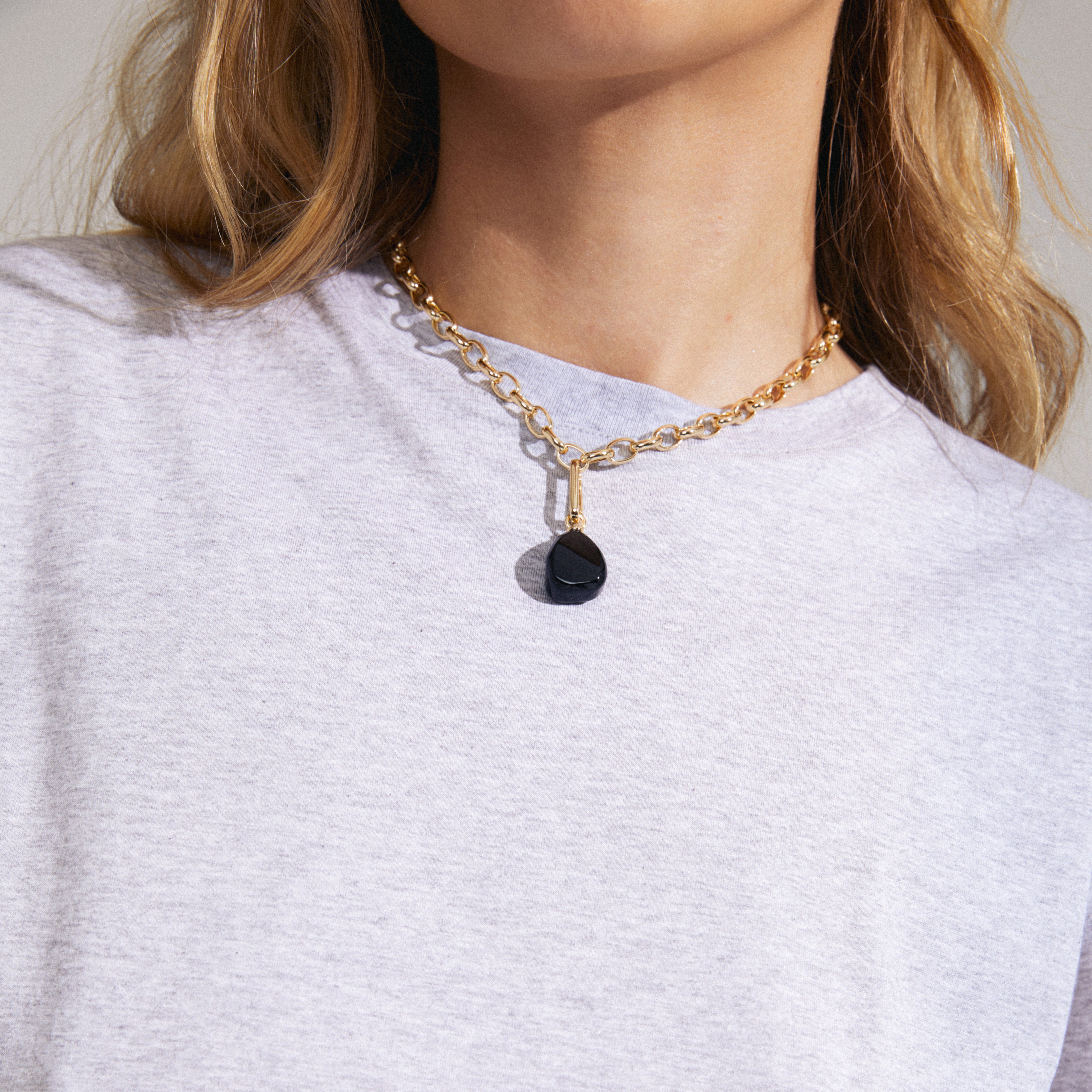 Woman wearing Pilgrim's CHARM black agate pendant, gold-plated, showcasing a unique semi-precious stone in a stylish, personalized design.