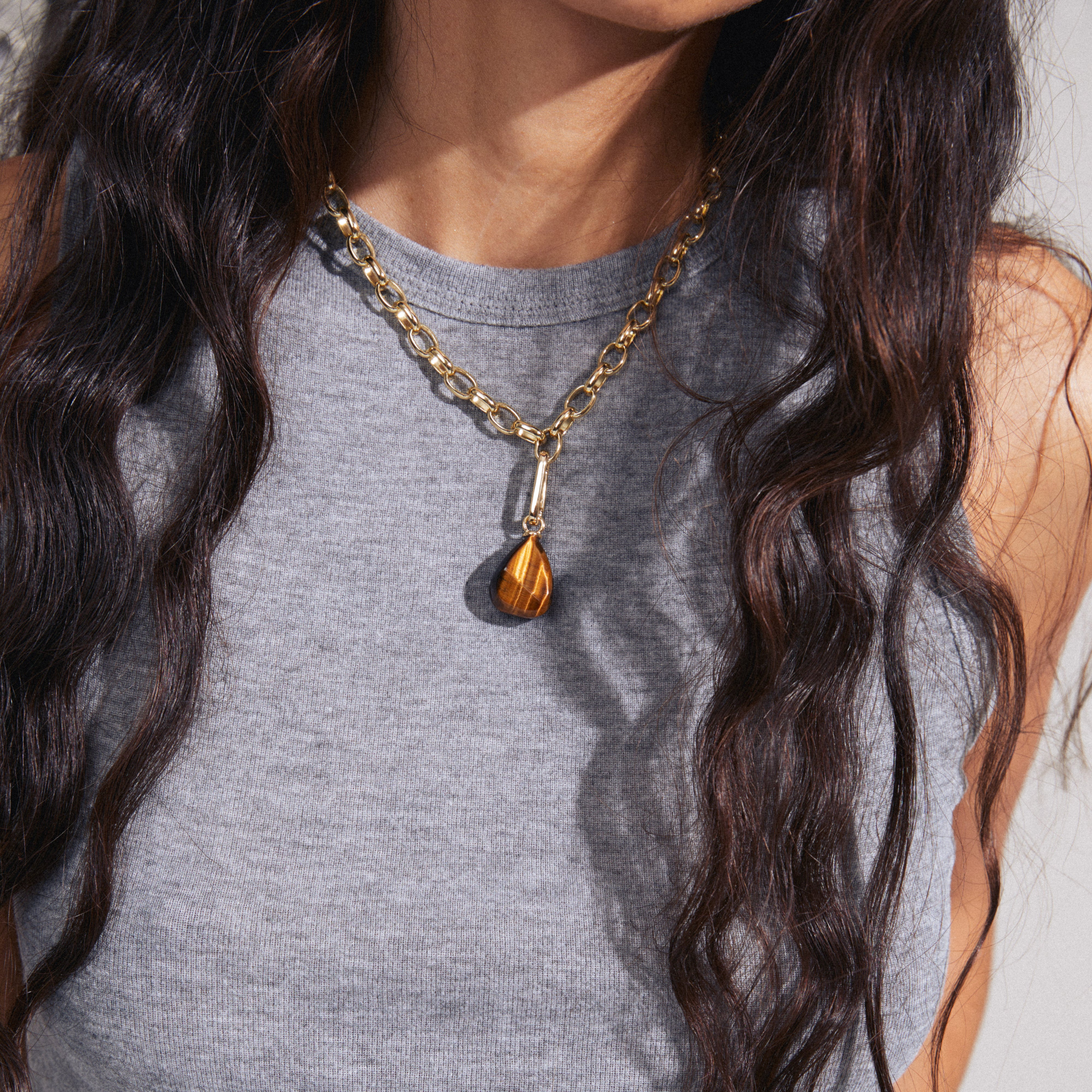 Woman wearing Pilgrim's CHARM tiger eye pendant, gold-plated, showcasing a semi-precious gemstone on an oval clasp, ideal for personalizing style with trendy jewelry.