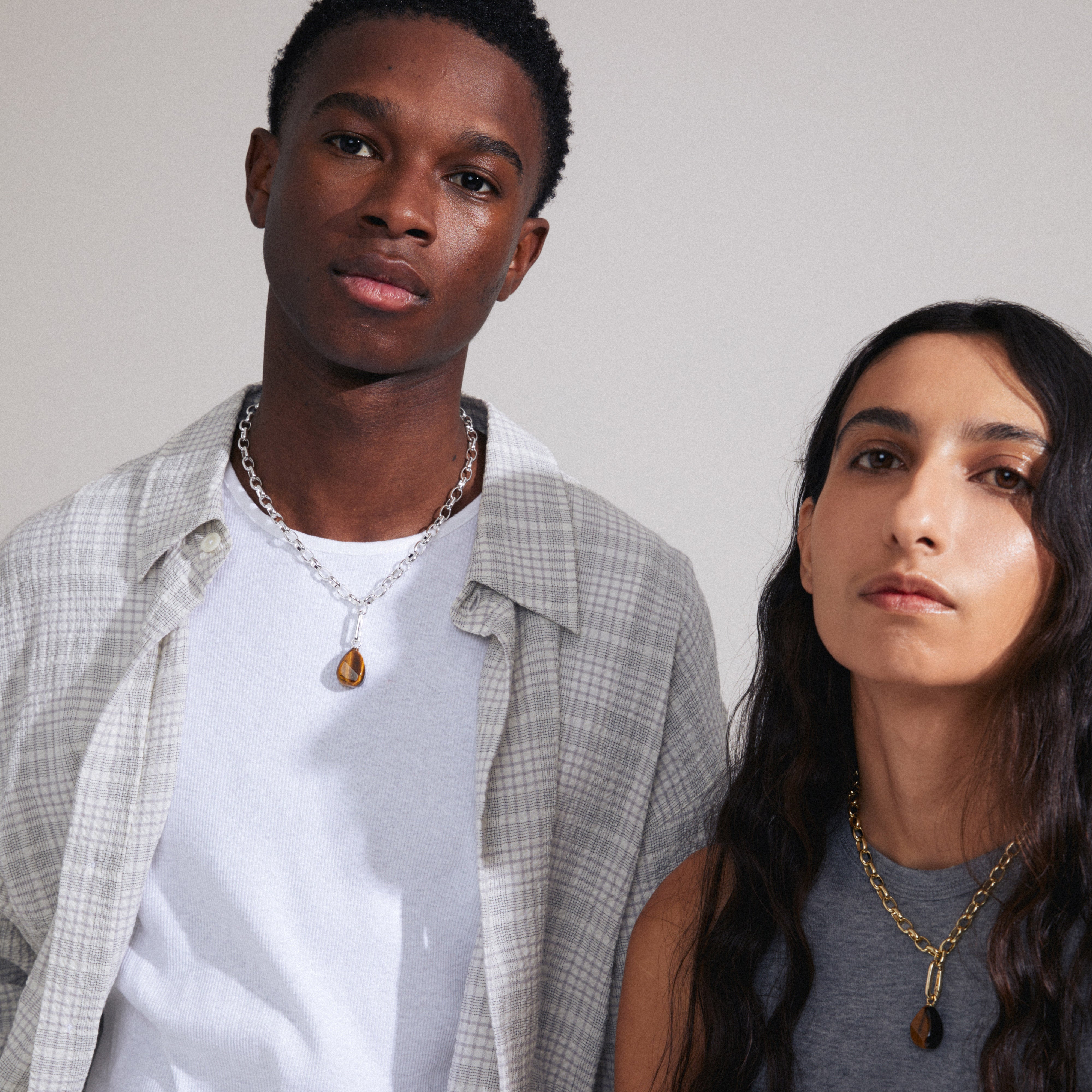 Man and woman showcasing Pilgrim's CHARM tiger eye pendant, gold-plated, offering a personalized touch with a semi-precious gemstone on a gold-plated clasp.