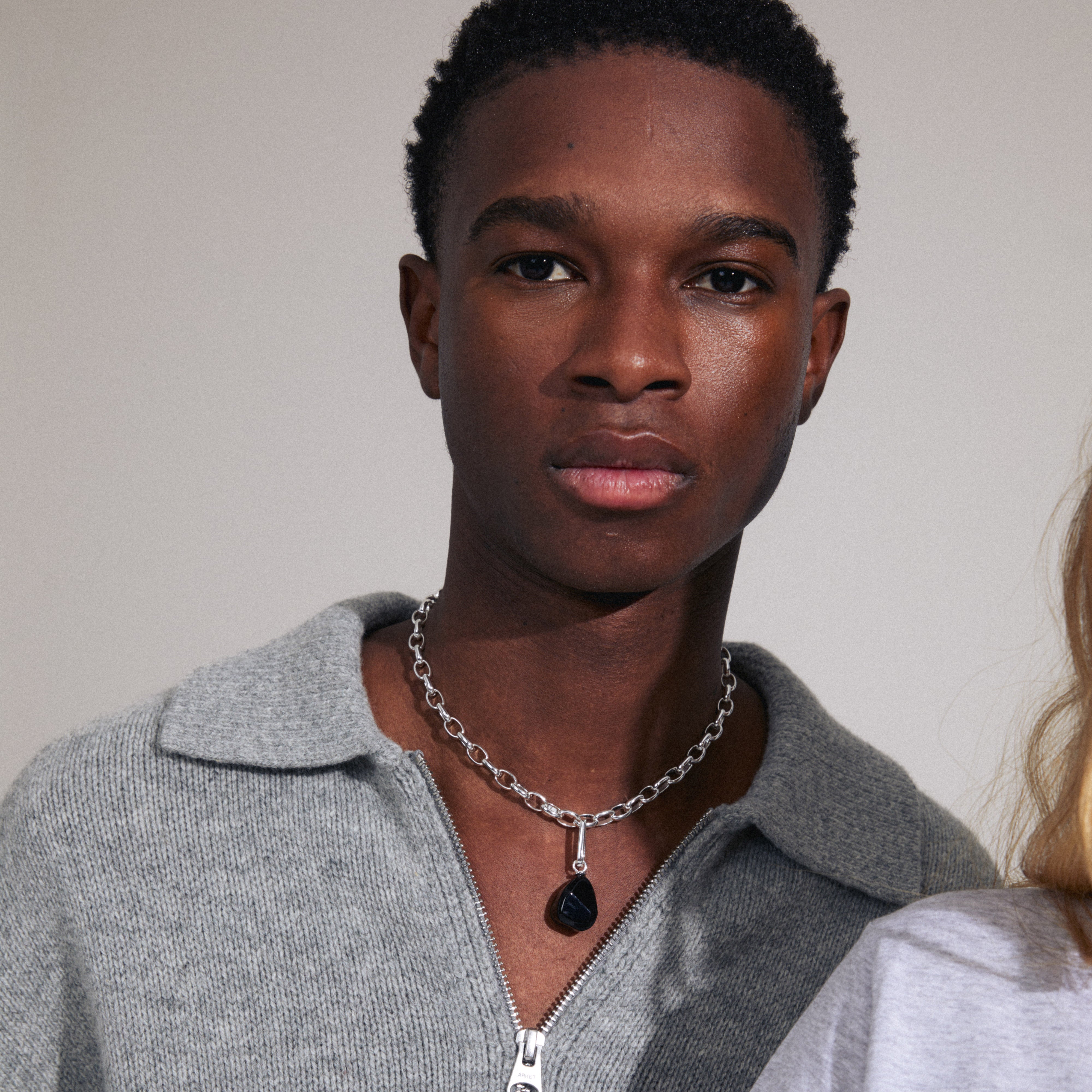 A man wearing the CHARM black agate pendant, silver-plated, showcasing a semi-precious stone in an oval carabiner, reflecting Pilgrim's unique and stylish design.