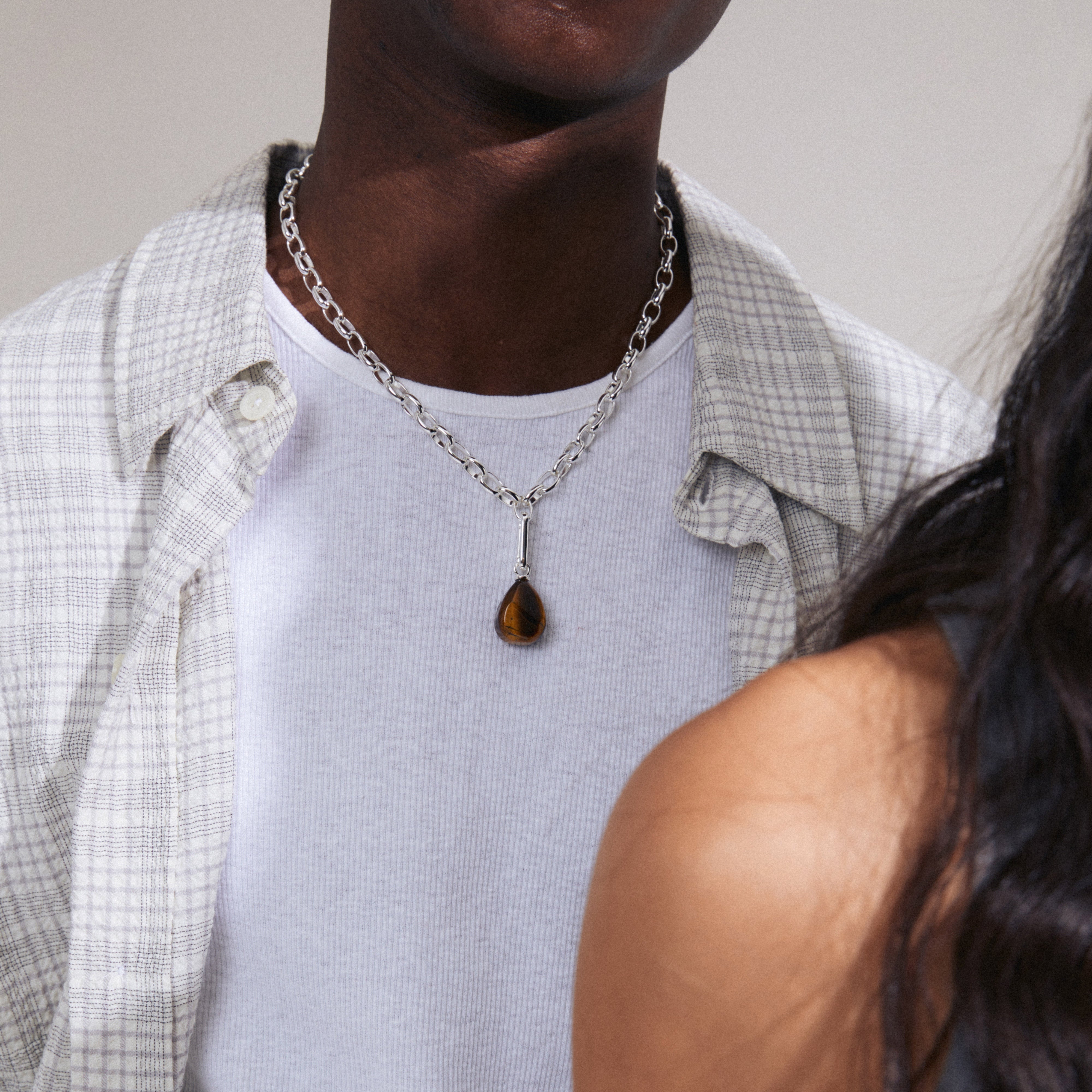 Man wearing silver-plated CHARM tiger eye pendant from Pilgrim, showcasing a semi-precious gemstone for personalized style.