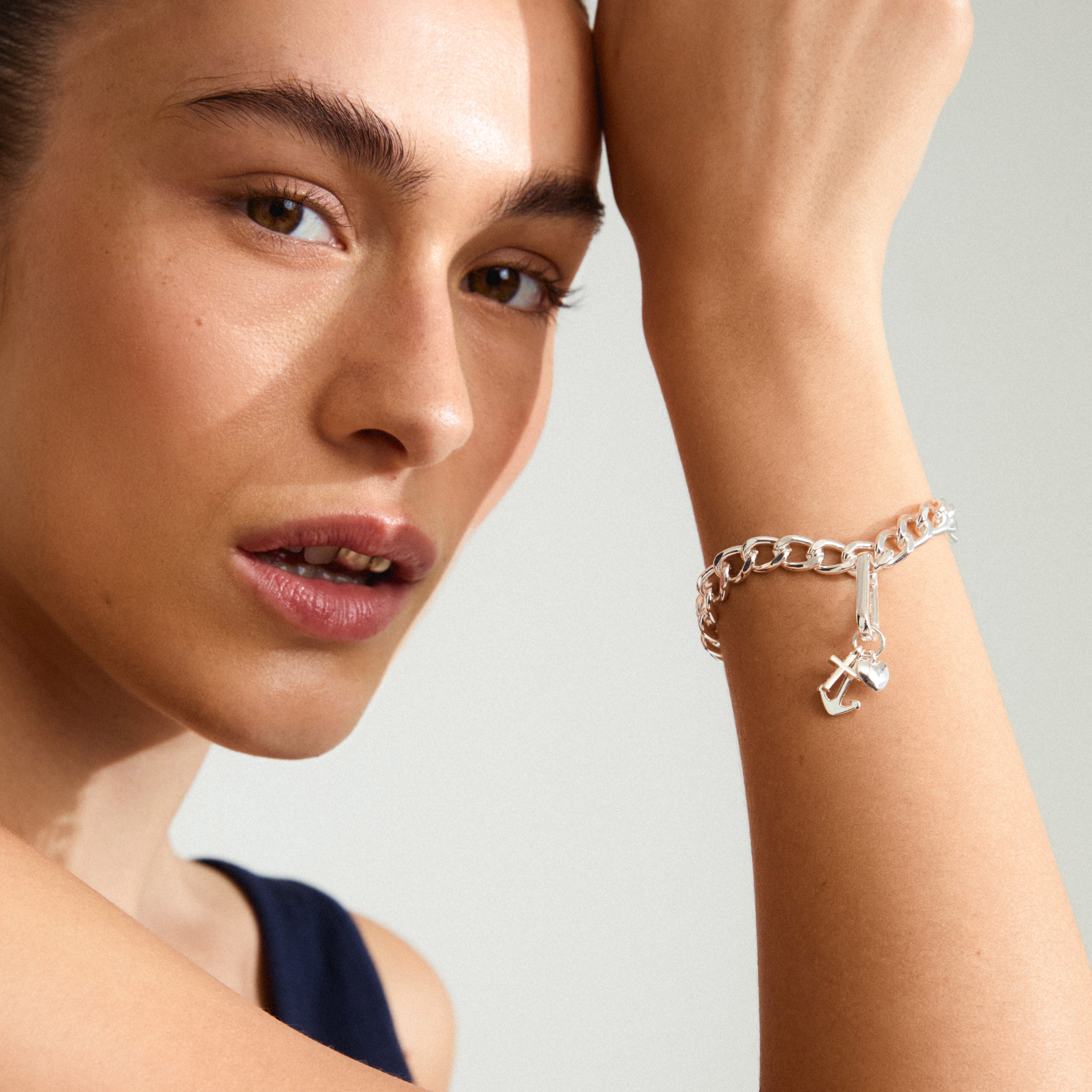 Silver-plated CHARM symbols pendant with cross, anchor, and heart, worn by a woman, offering a touch of elegance and personal significance.