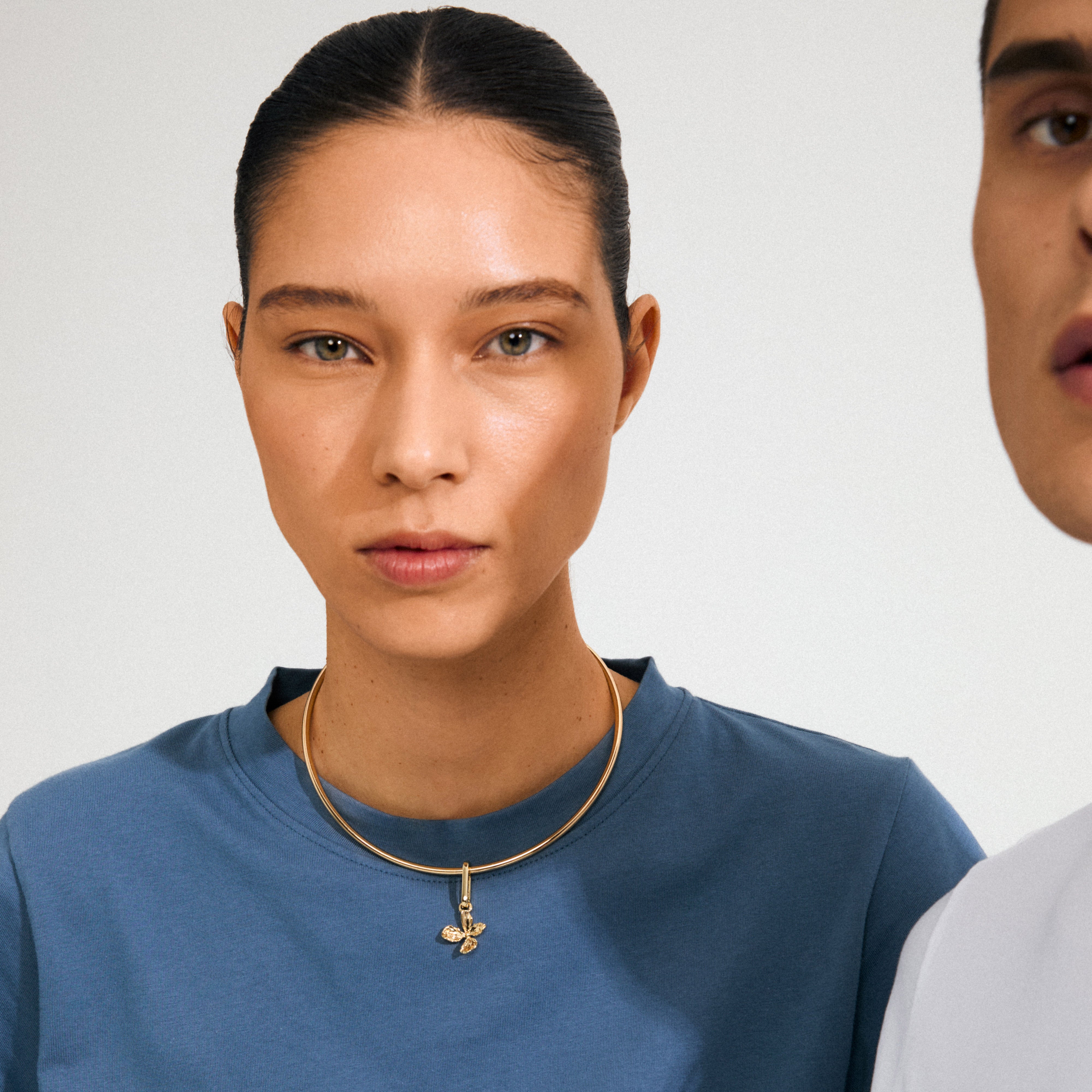 Young woman showcases Pilgrim's CHARM flower pendant, gold-plated, on a slender choker, embodying a sweet boho vibe against a minimalist background.