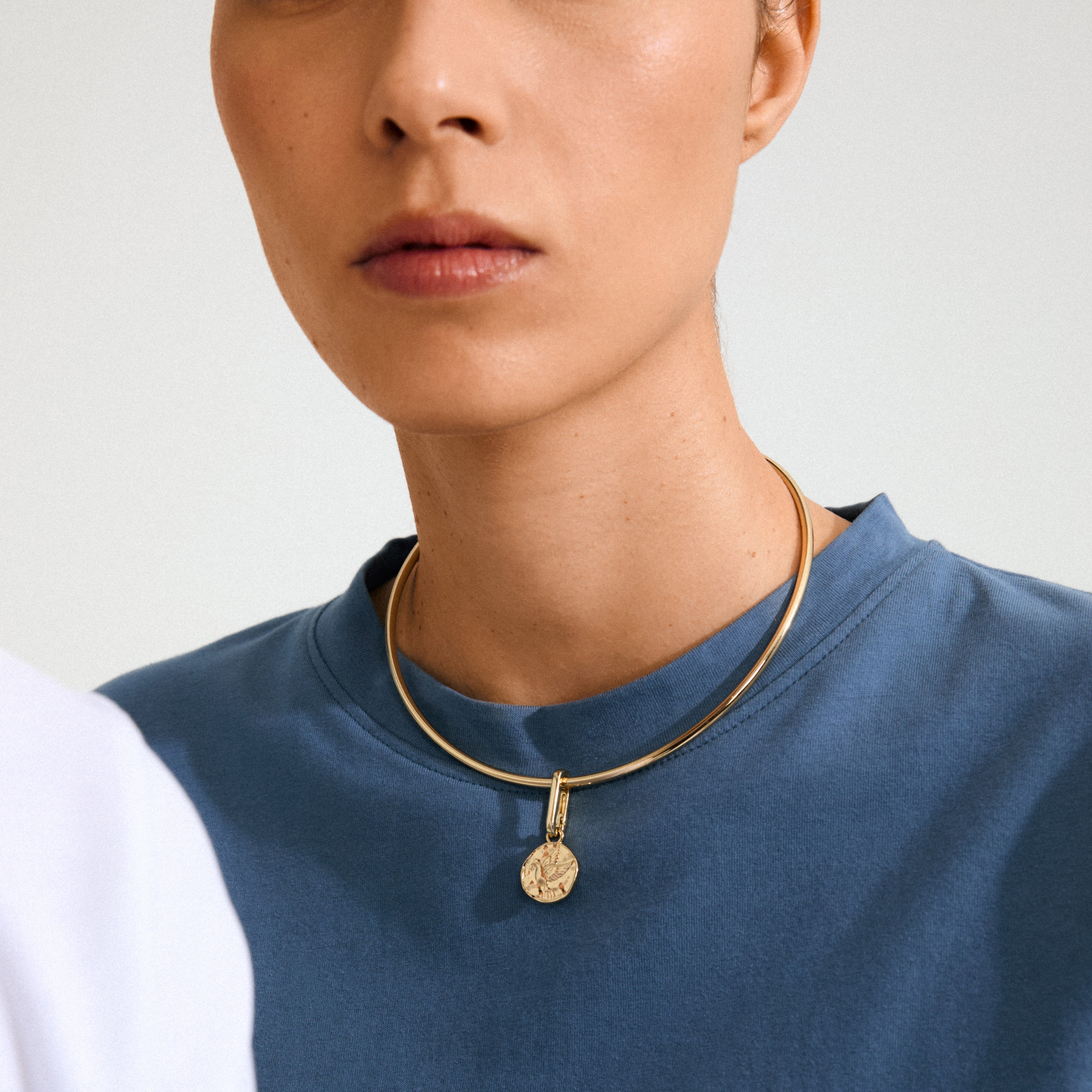 Close-up of a person wearing Pilgrim's CHARM gold-plated peace dove pendant on a chunky torque choker, embodying calm and personal style.