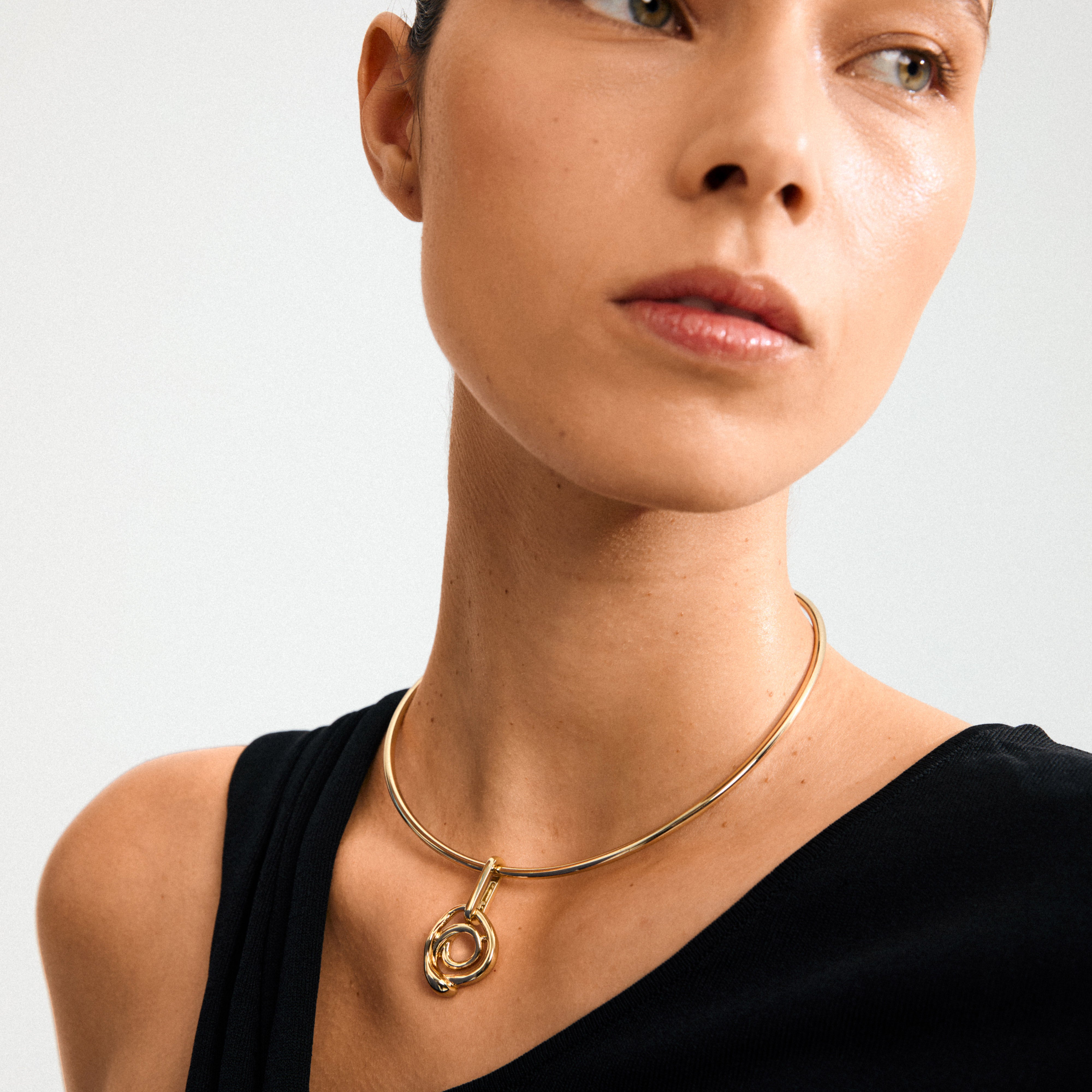Woman wearing Pilgrim's CHARM curl pendant, a gold-plated abstract loop on a sleek choker, highlighting creative style and craftsmanship with a Scandinavian touch.
