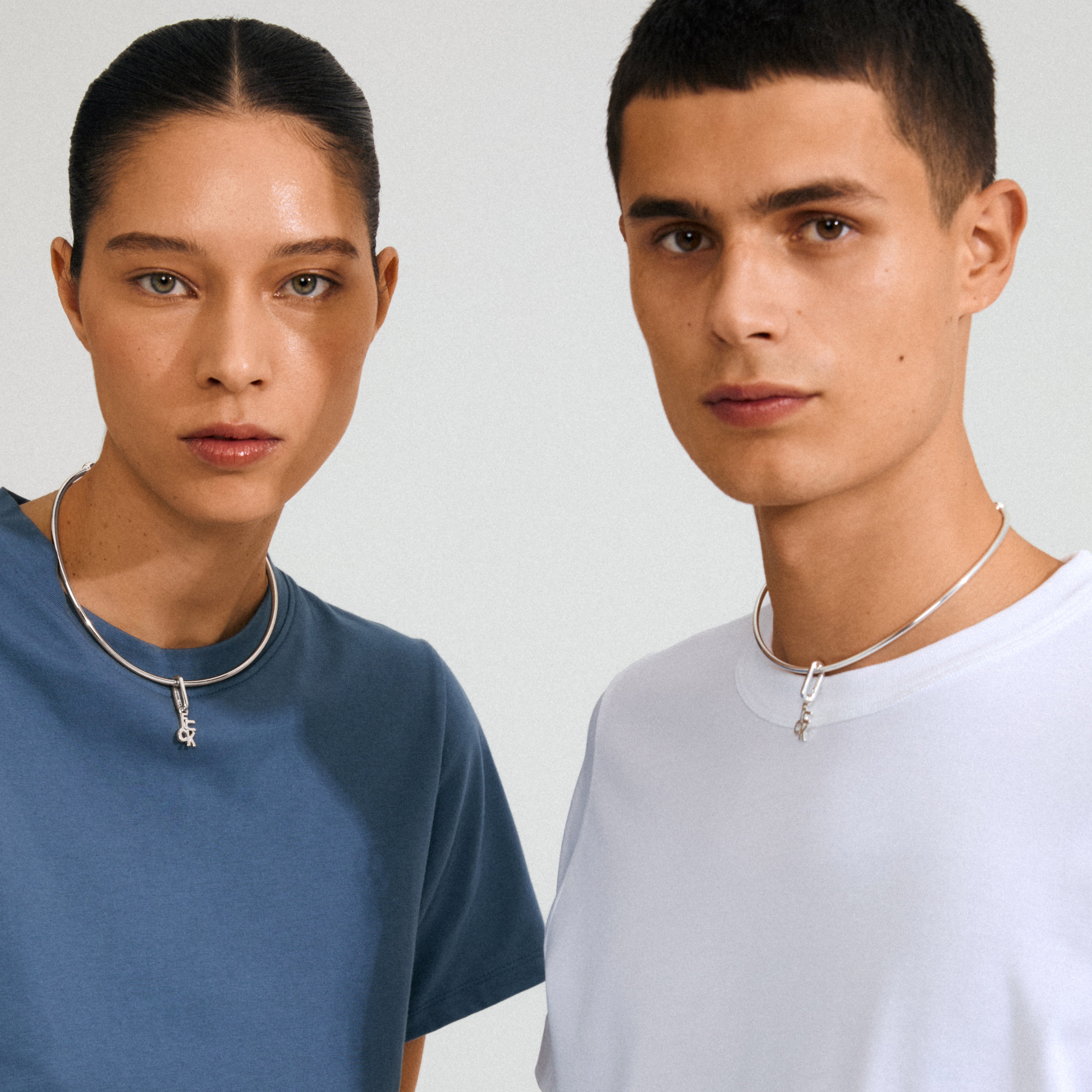 Two young adults model Pilgrim's CHARM f... silver-plated pendant, showcasing its edgy, recycled design with a padlock charm on matching chunky necklaces.