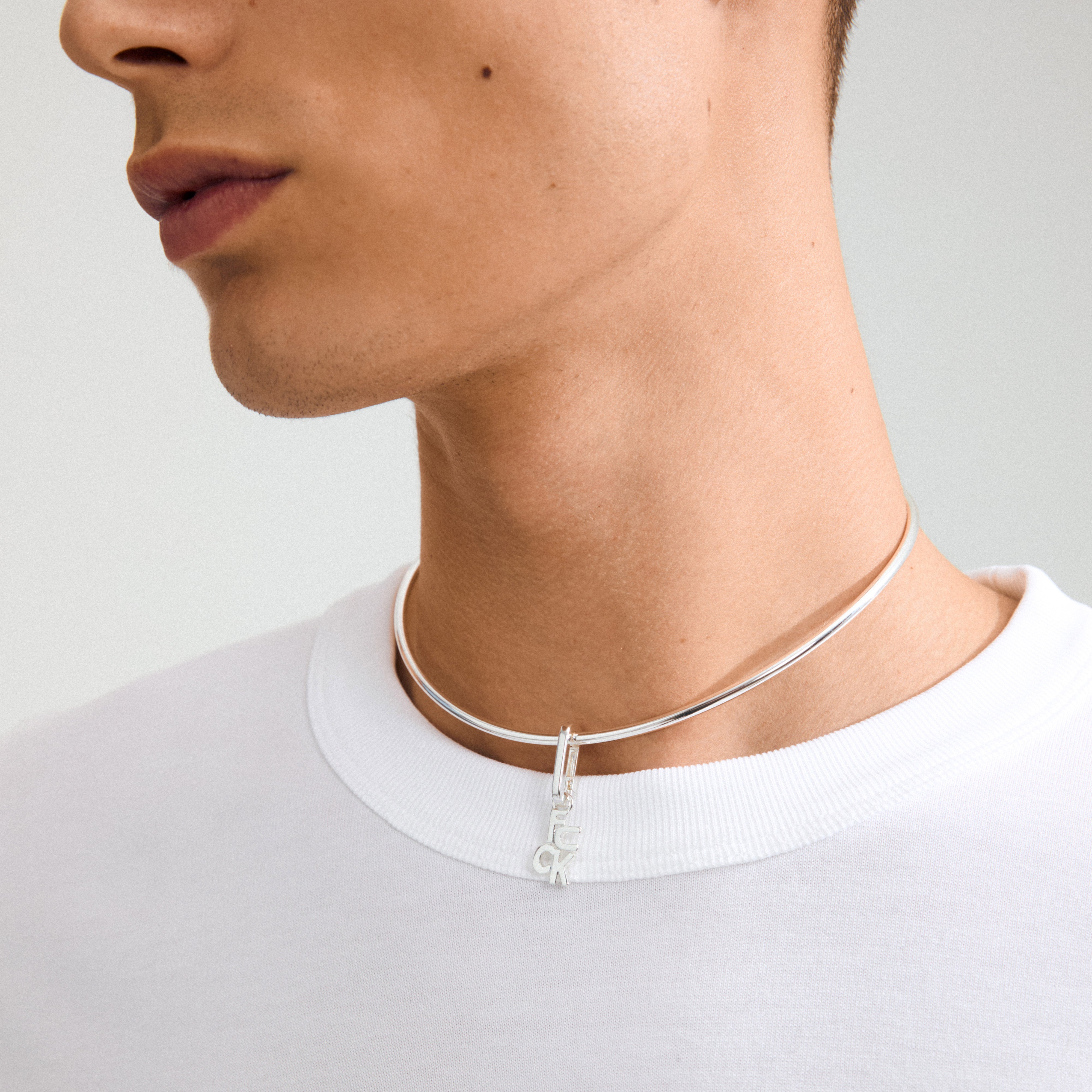 Close-up of Pilgrim's silver-plated CHARM f... pendant necklace, featuring bold letter design, adding an edgy twist to a simple white t-shirt.
