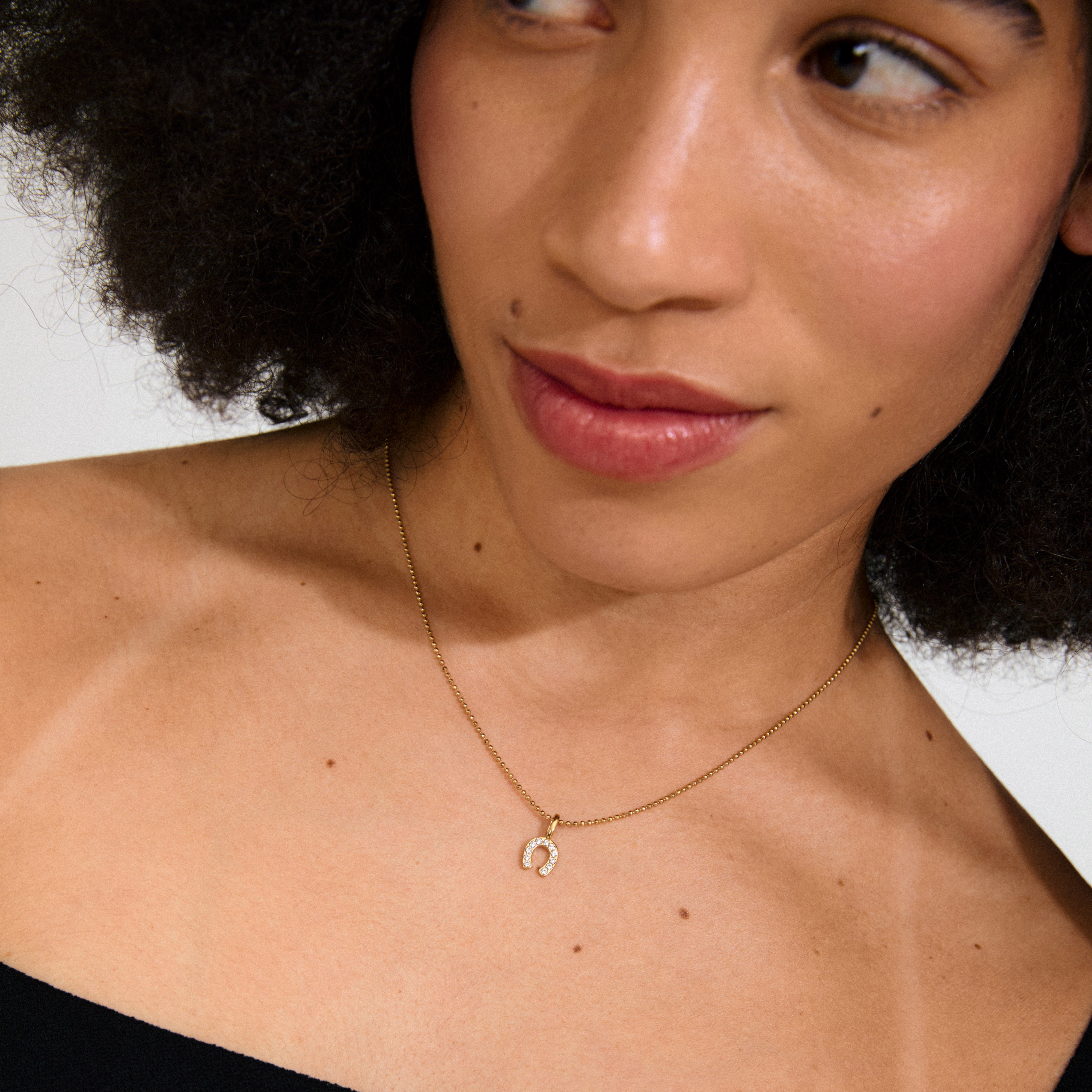 Gold-plated CHARM mini horseshoe pendant with sparkling crystals, perfect for adding a unique touch to hoops, necklaces, or bracelets. Fashionable and eco-friendly.
