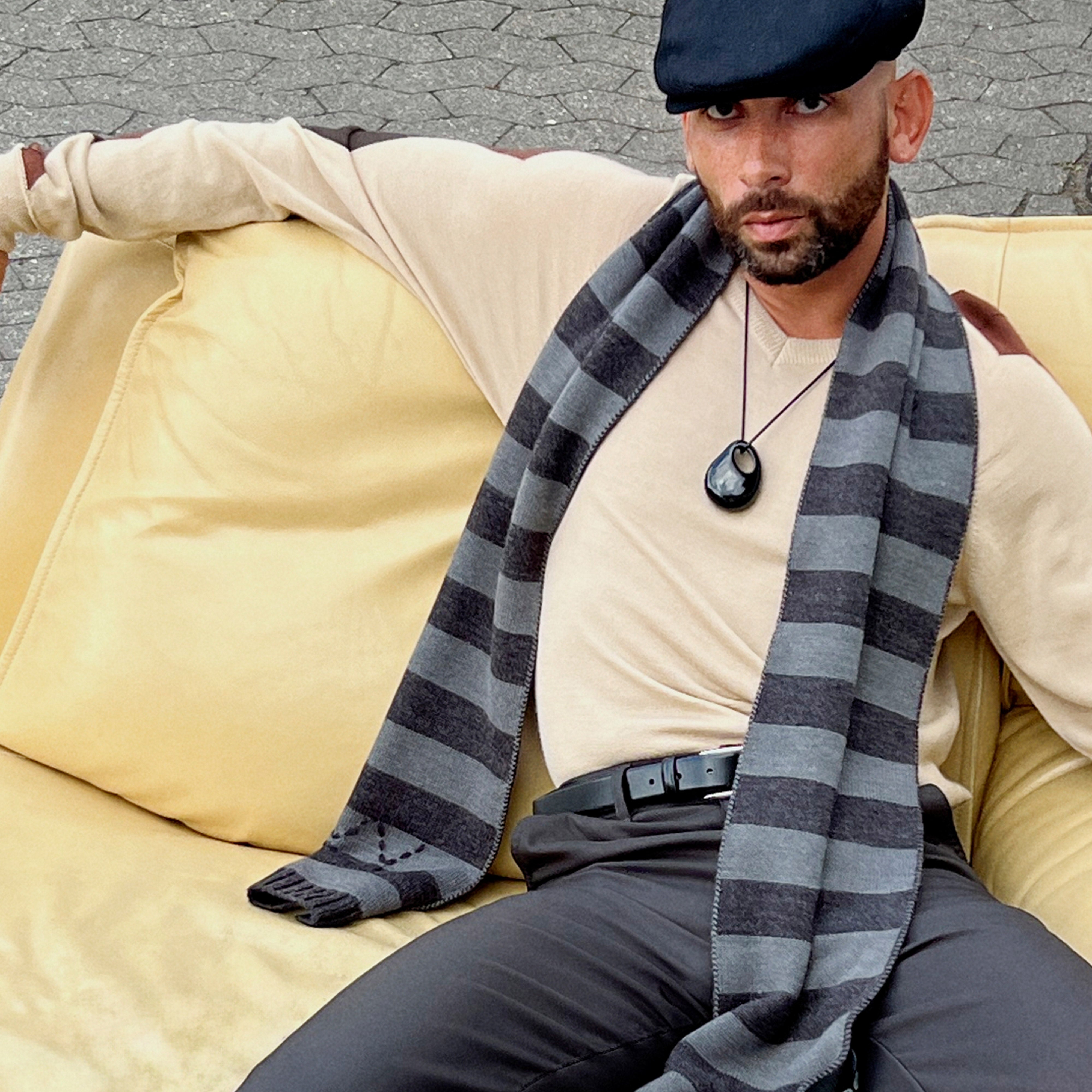 Man sitting on a couch wearing the FREJA WEWER x PILGRIM Polpo necklace with a large recycled black acrylic pendant on a fabric cord.
