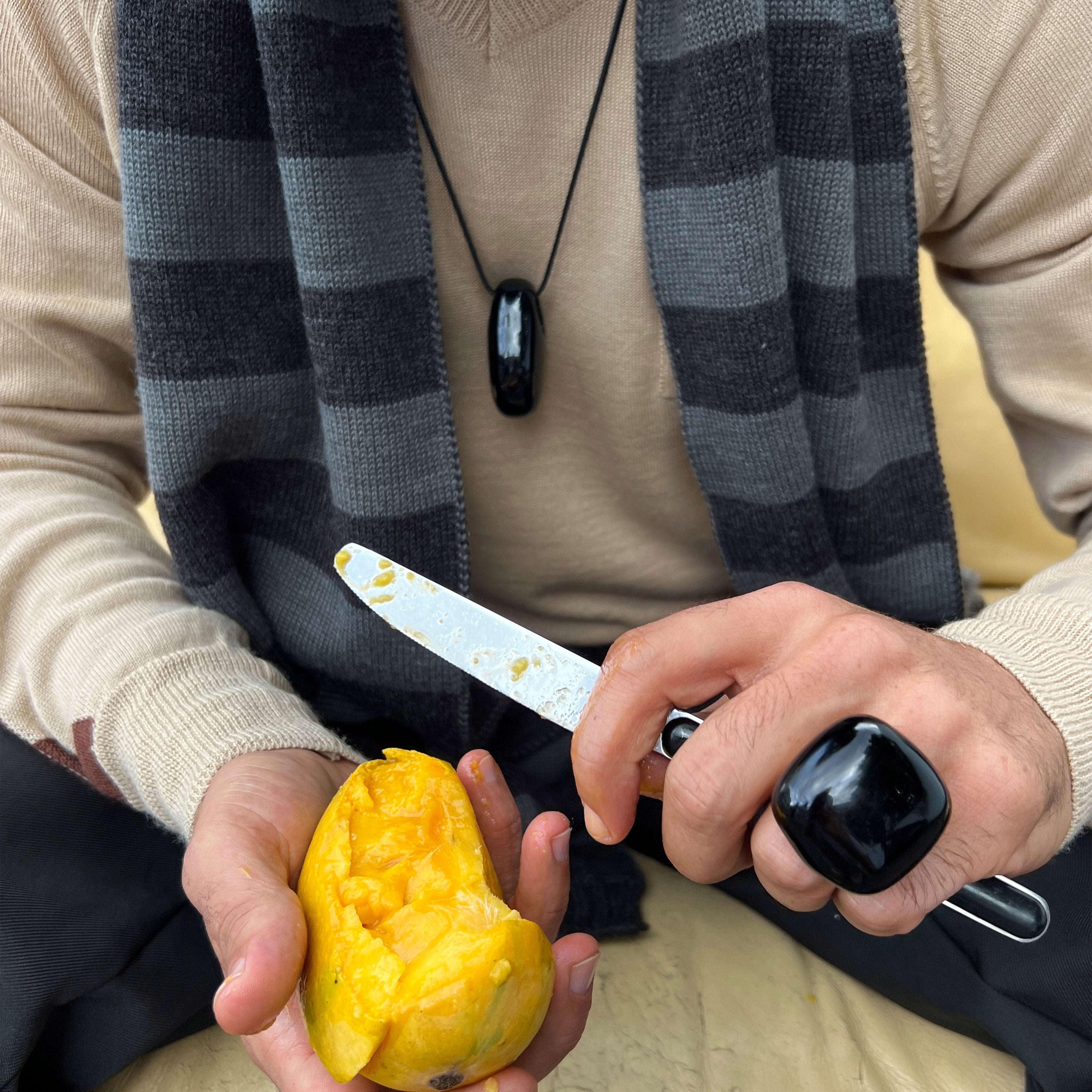 FREJA WEWER x PILGRIM Polpo necklace, a black recycled acrylic pendant on a customizable cord, shown being held alongside a knife and fruit.