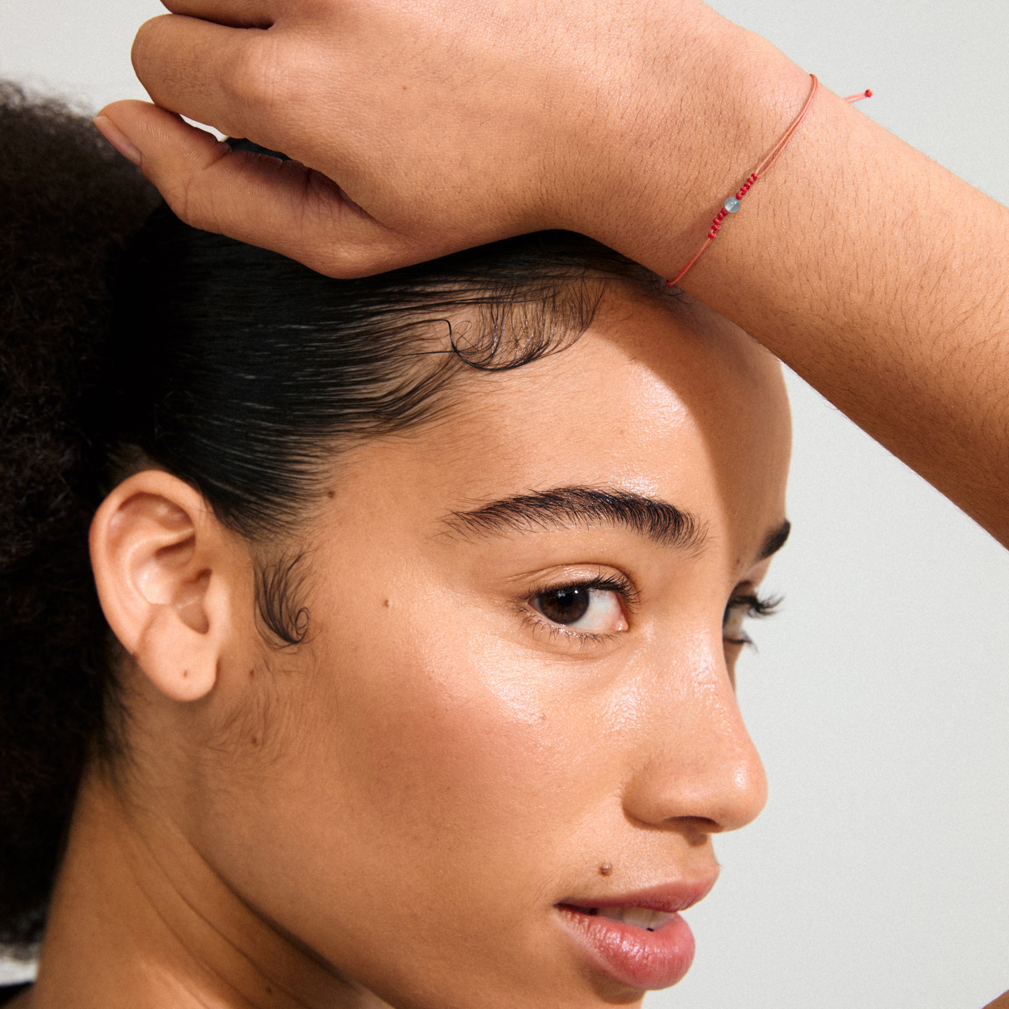 Close-up of a woman's face wearing the MARCH birthstone bracelet, featuring a red cotton cord and Aquamarine stone for a boho style.