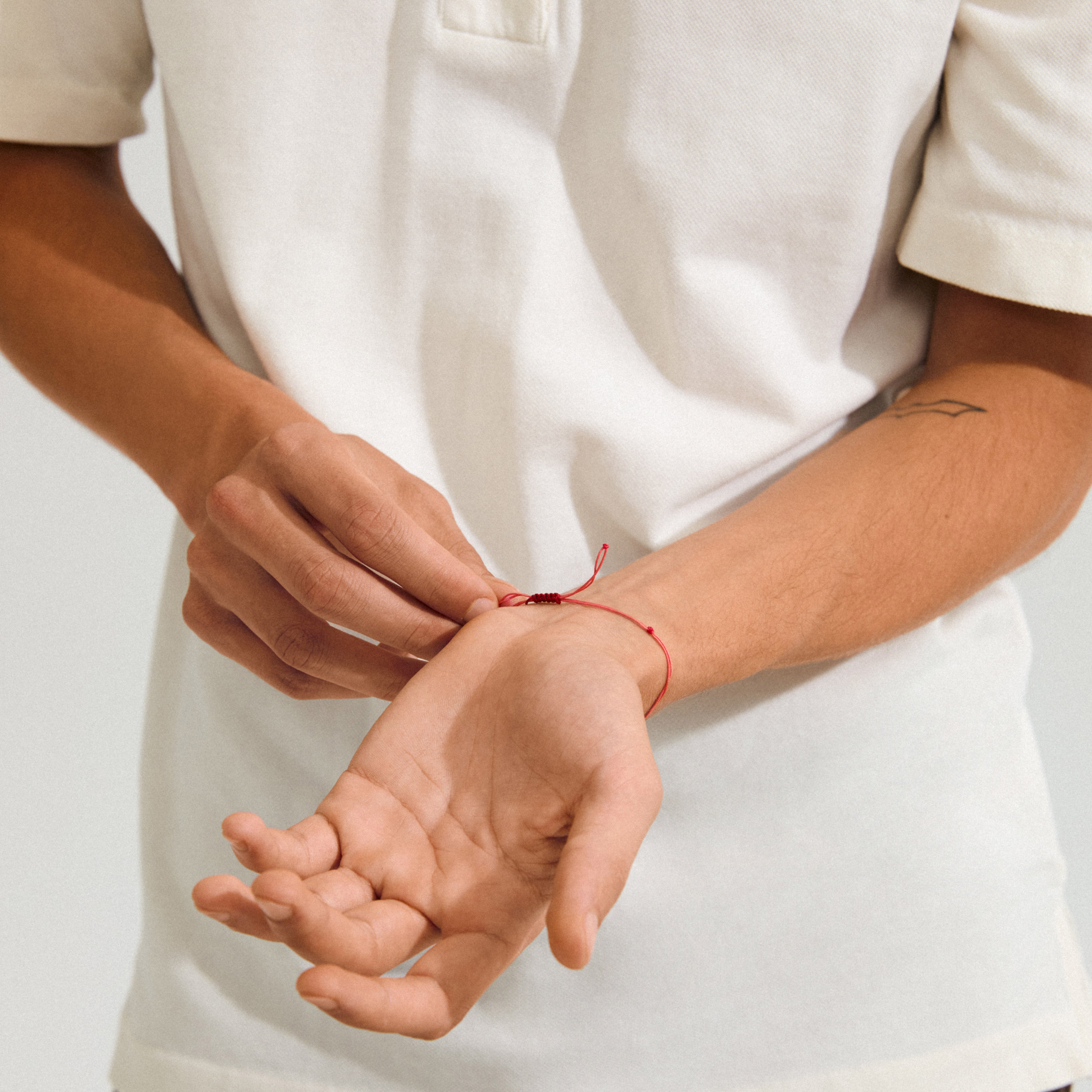 Person tying a red string bracelet with aquamarine on wrist, showcasing the MARCH birthstone bracelet's delicate design and adjustable closure.