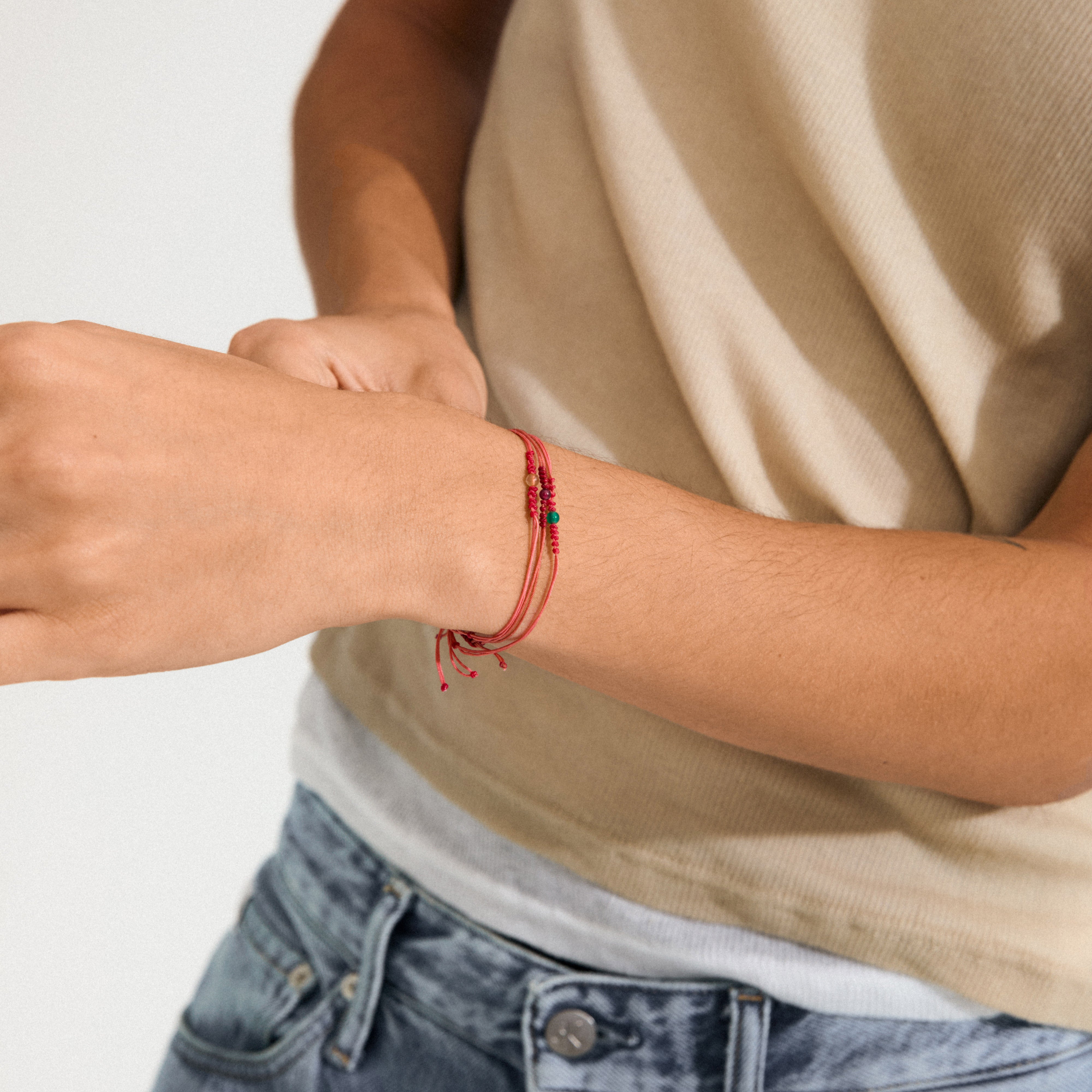 Close-up of a person wearing the MARCH birthstone bracelet on their left wrist, featuring red cord and Aquamarine, symbolizing calm and balance.