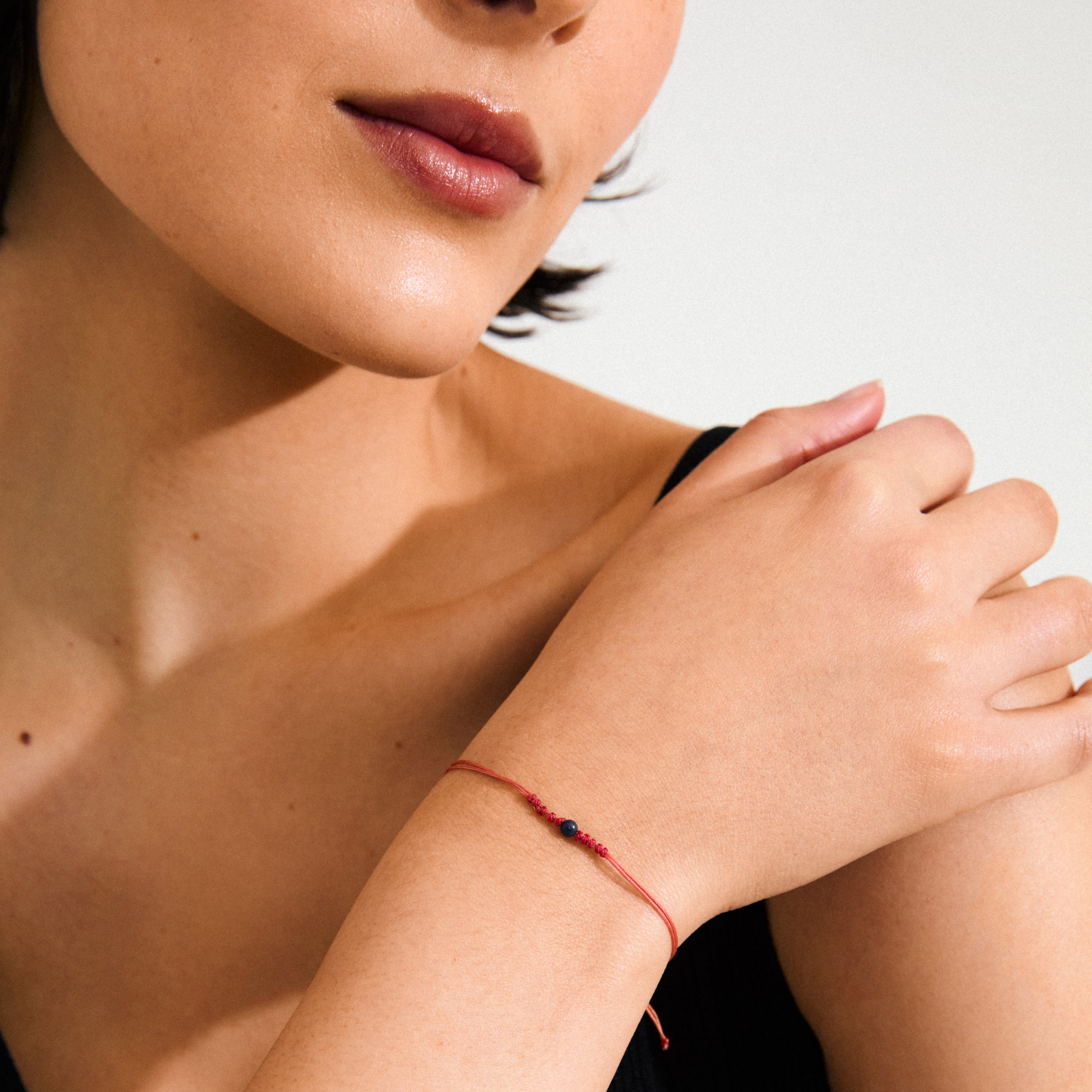 SEPTEMBER birthstone bracelet featuring a red cotton cord with a blue Lapis bead, elegantly displayed on a woman's wrist for a boho-chic look.