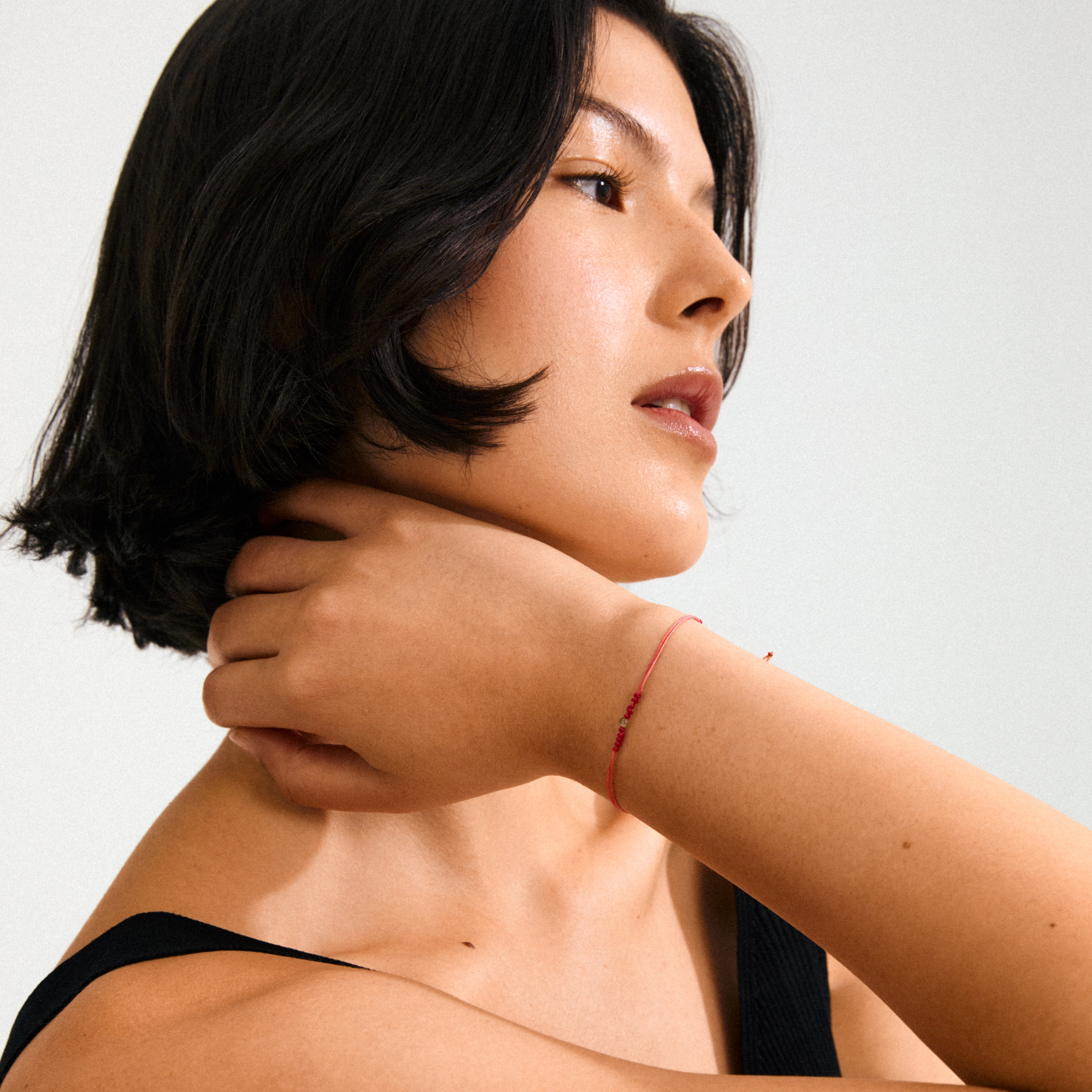A woman models the AUGUST birthstone bracelet, featuring red cotton cord and a small Peridot stone, symbolizing happiness and joy.