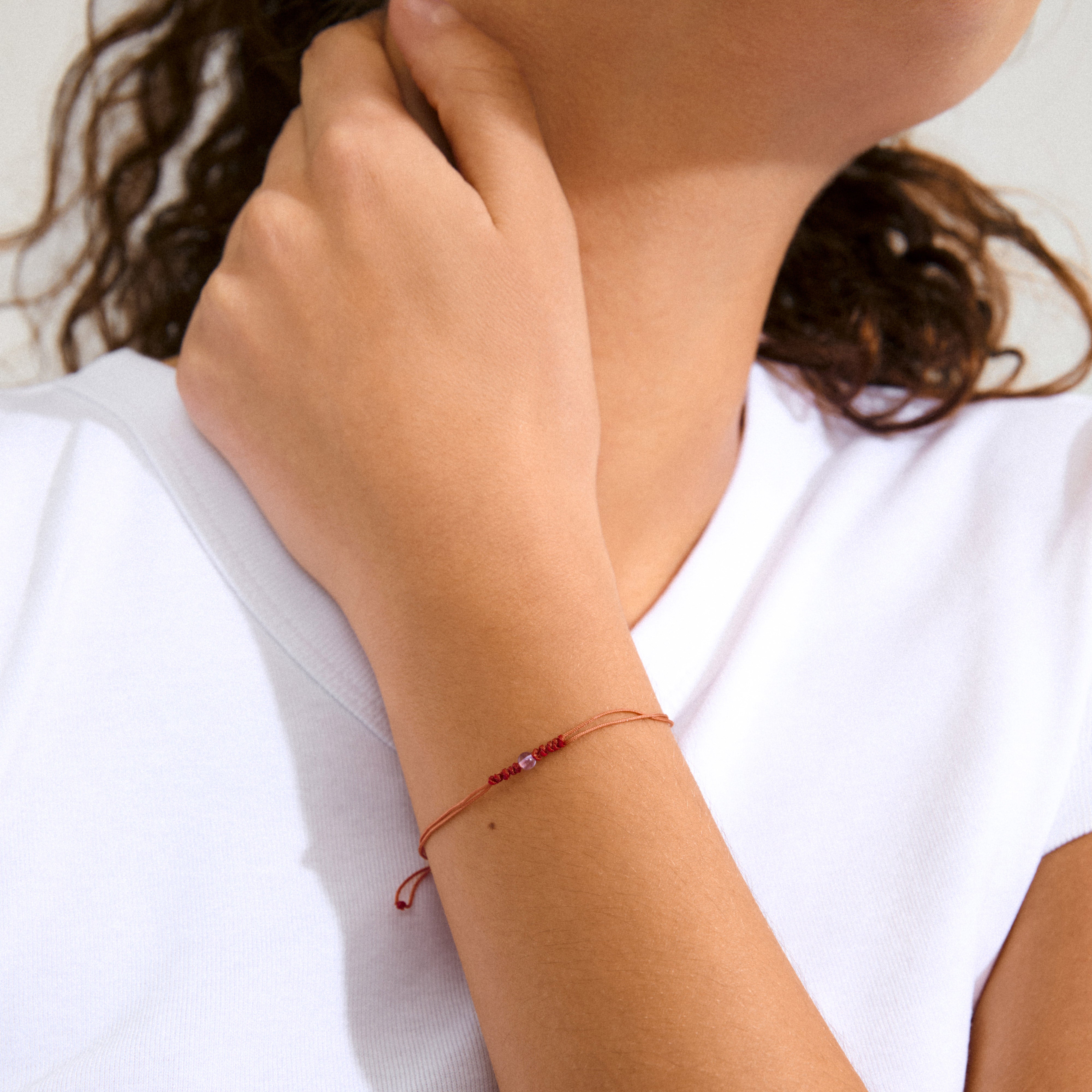 Close-up of a woman's wrist wearing the FEBRUARY birthstone bracelet, featuring a delicate red cotton cord and Amethyst, symbolizing serenity and harmony.