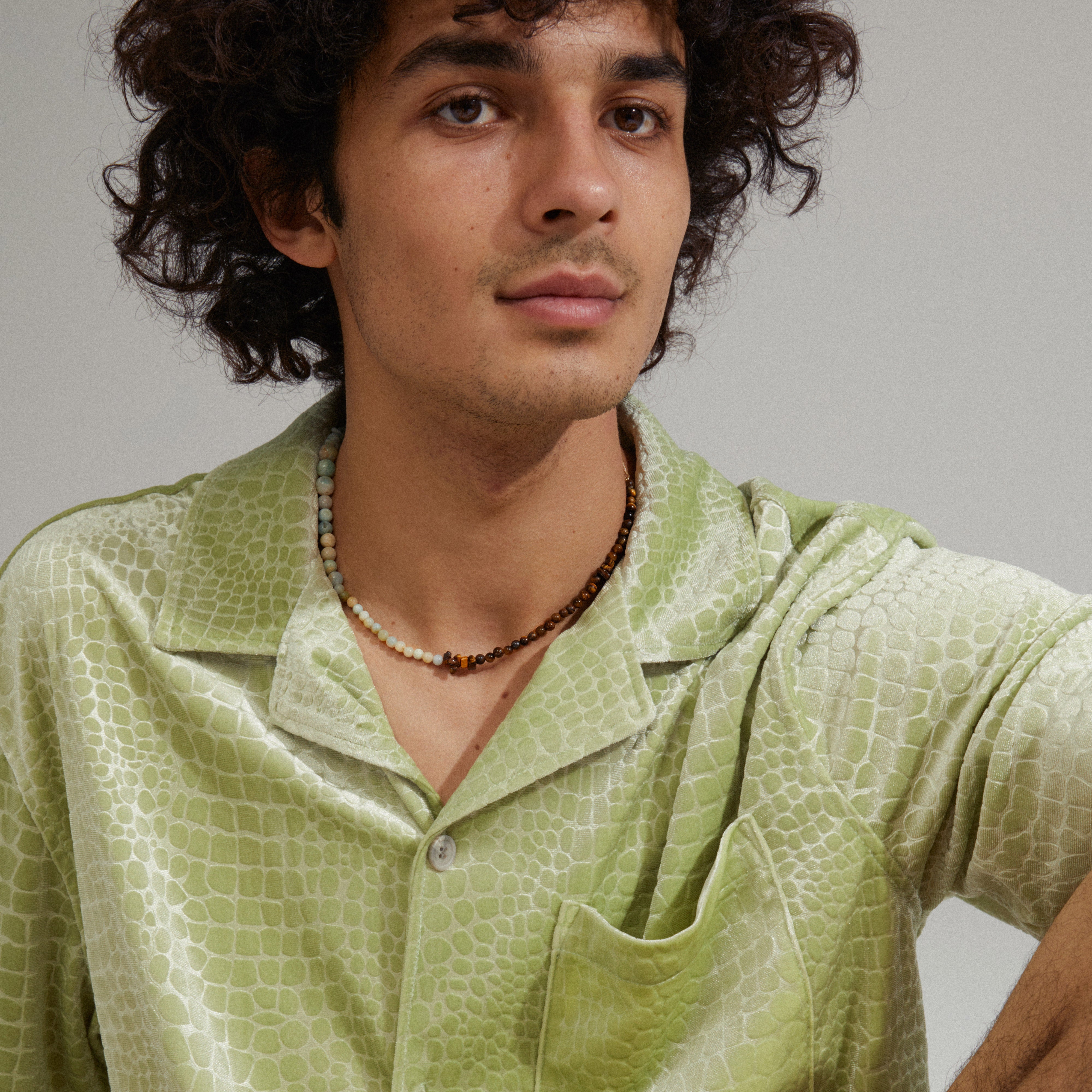 SOULMATES necklace mint/gold-plated featuring amazonite and tiger eye stones, worn by a man in a green shirt, showcasing its unique asymmetrical design.