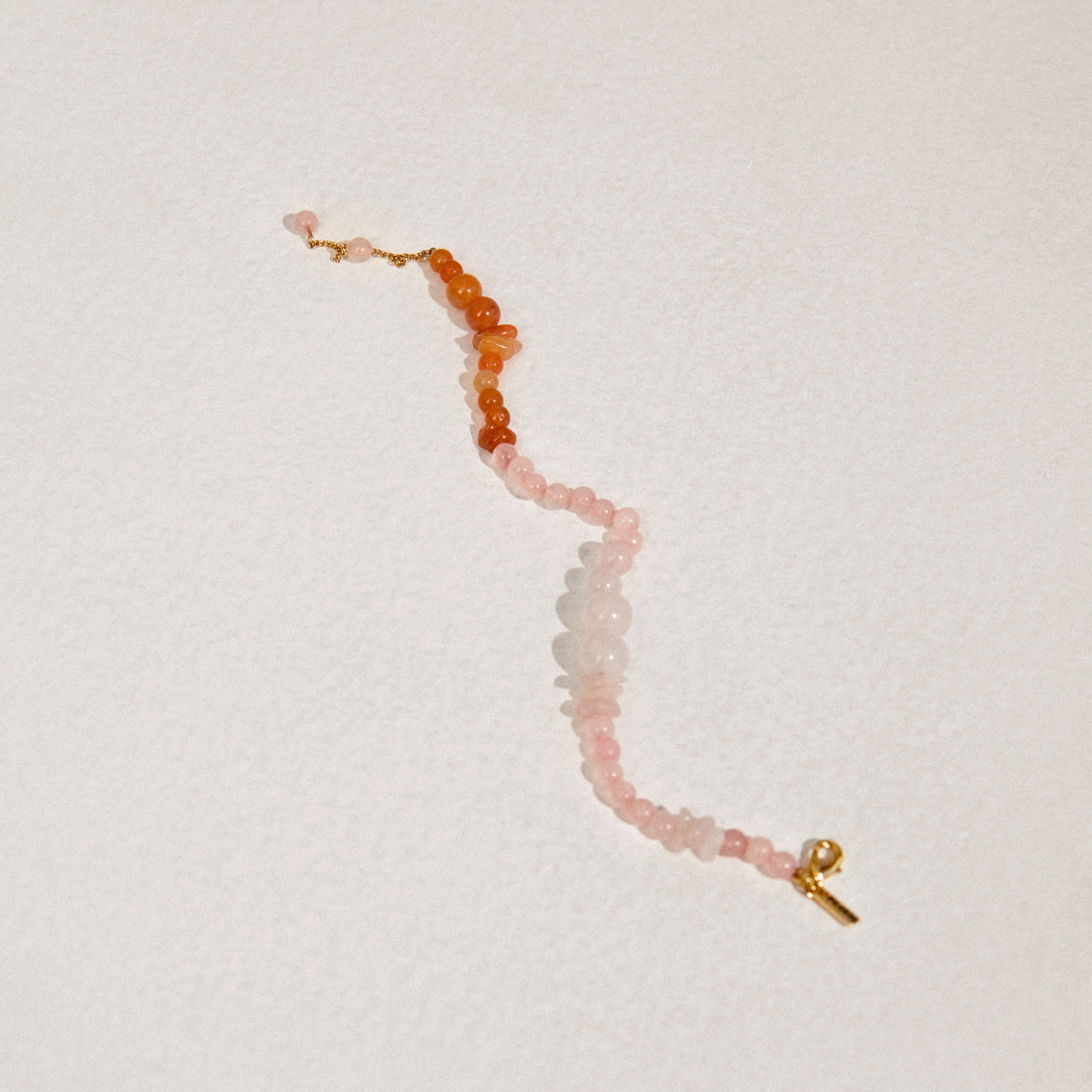 SOULMATES bracelet rose/gold-plated featuring asymmetrical rose quartz and red aventurine beads, showcasing delicate pink and orange-red hues on a white surface.