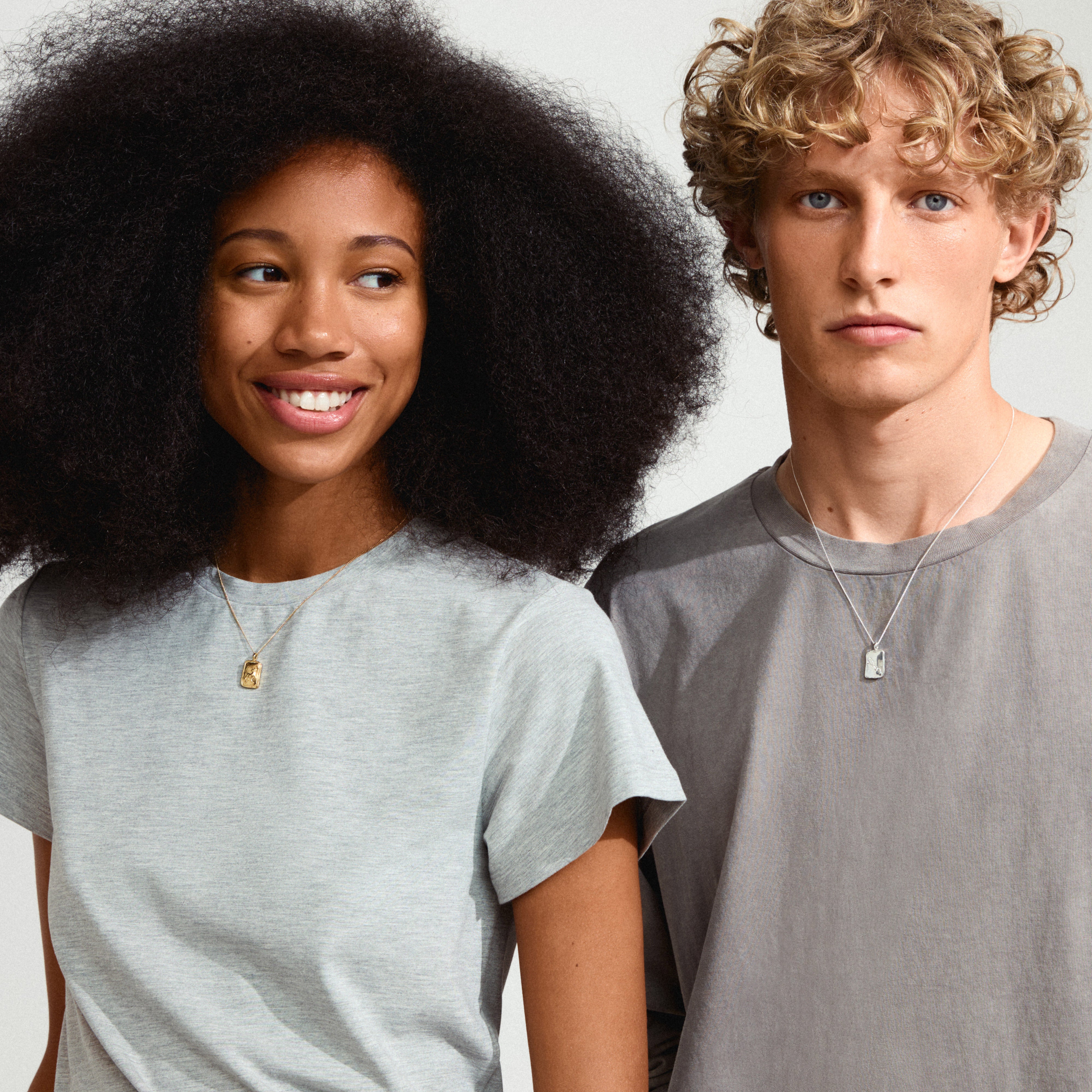 TAURUS Zodiac Sign necklace, gold-plated, featuring a rustic, handcrafted square coin pendant with dual zodiac and constellation designs, worn by a man and woman.