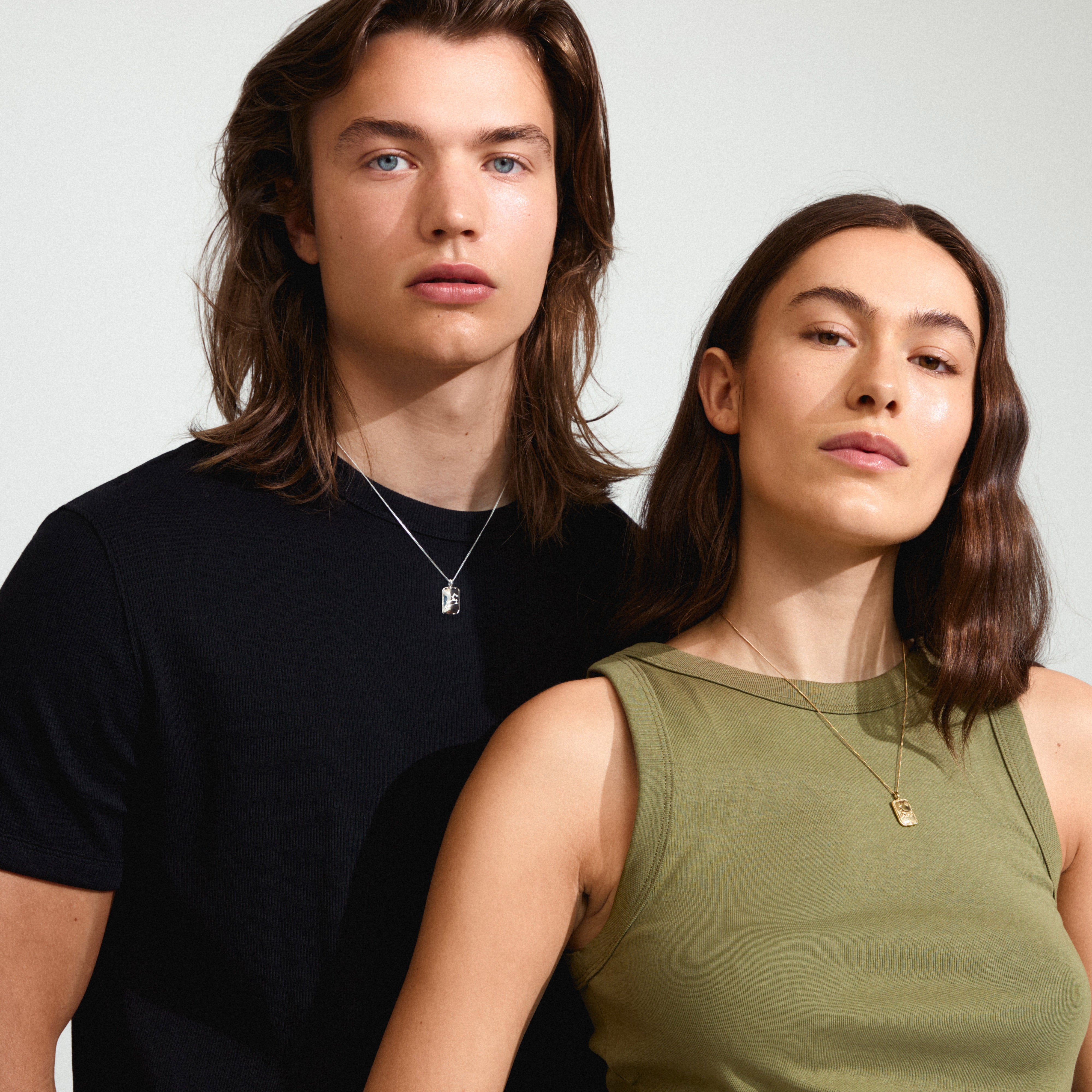 LEO Zodiac Sign necklace, gold-plated, worn by a man with long hair. Features a square coin pendant with a dual design, showcasing a Leo motif and constellation.