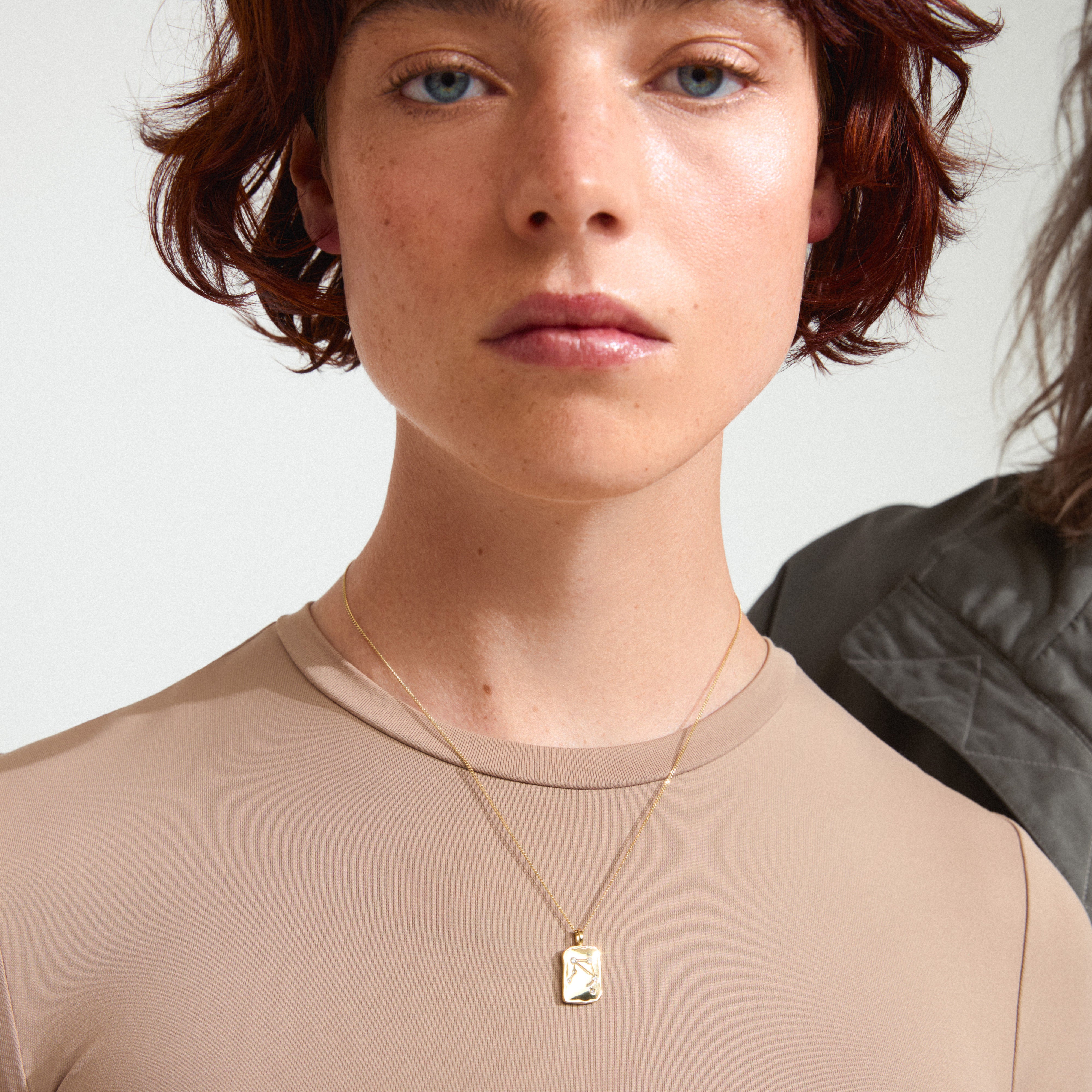 Woman with short red hair wearing the LIBRA Zodiac Sign necklace by Pilgrim, featuring a gold-plated coin pendant with Libra motif and sparkling constellation.