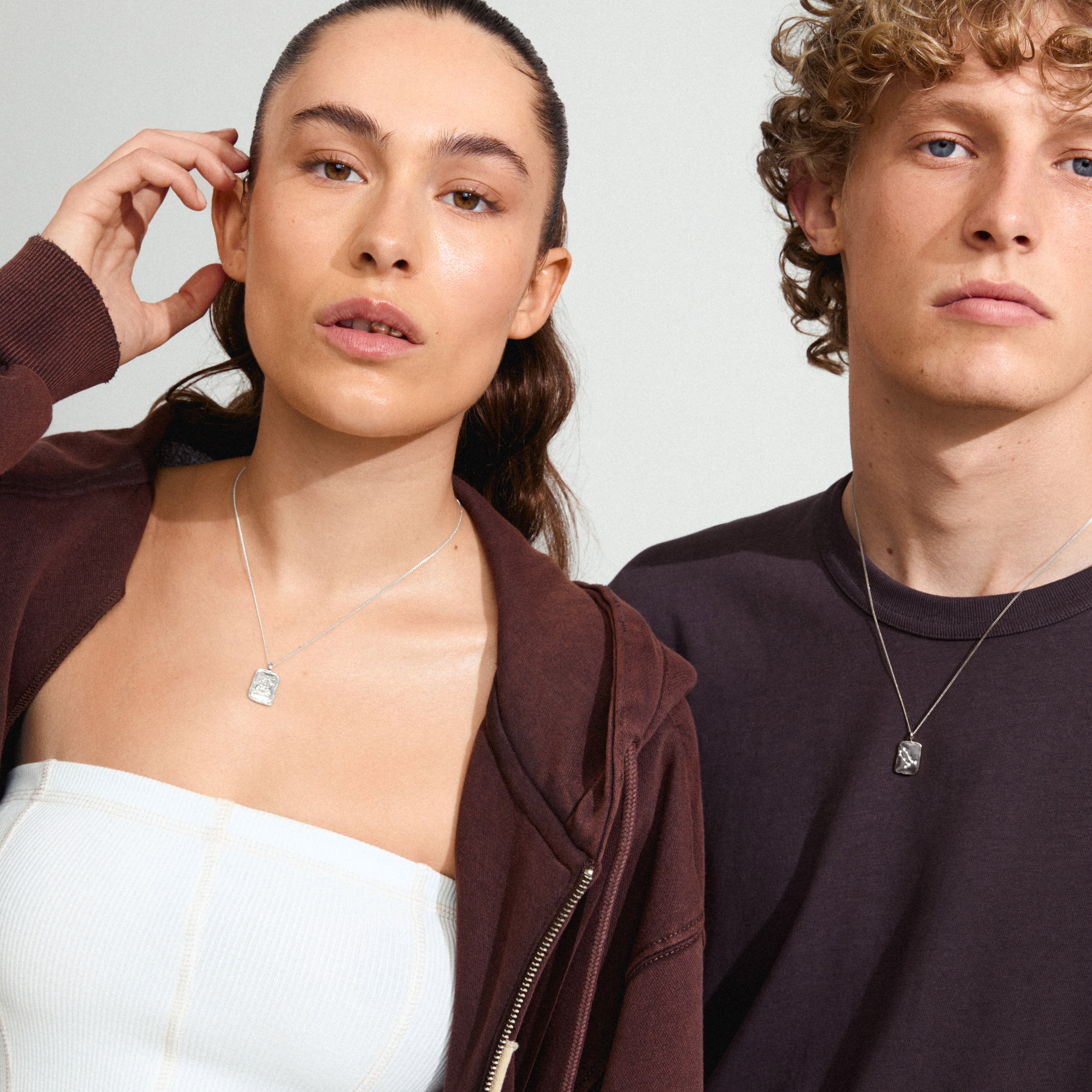 GEMINI Zodiac Sign necklace, silver-plated, featuring a reversible square coin pendant with zodiac and sparkling constellation designs, worn by a man and woman.