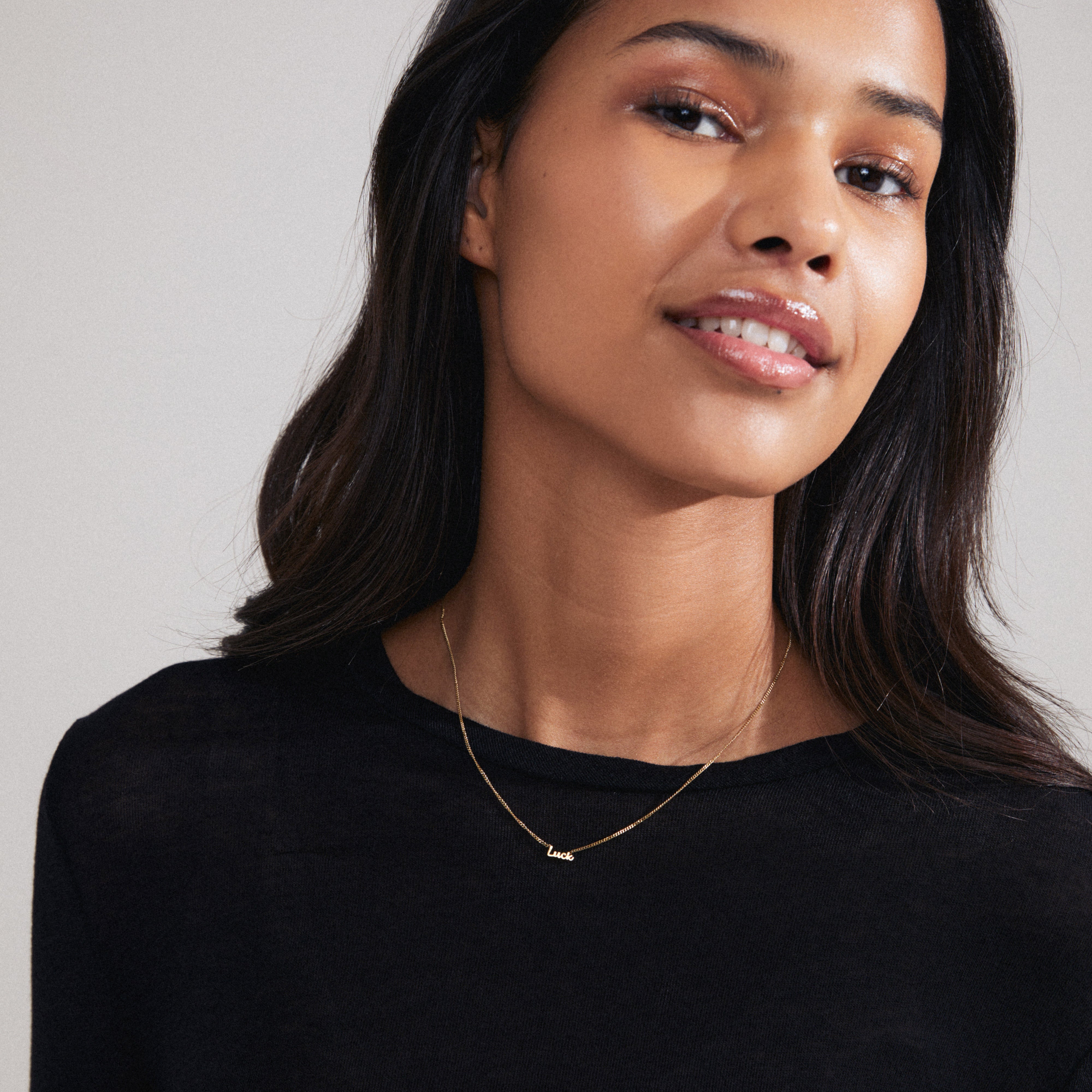 Woman wearing LUCK necklace, a gold-plated, cursive script pendant on a chain, embodying personal style and Scandinavian craftsmanship by Pilgrim.