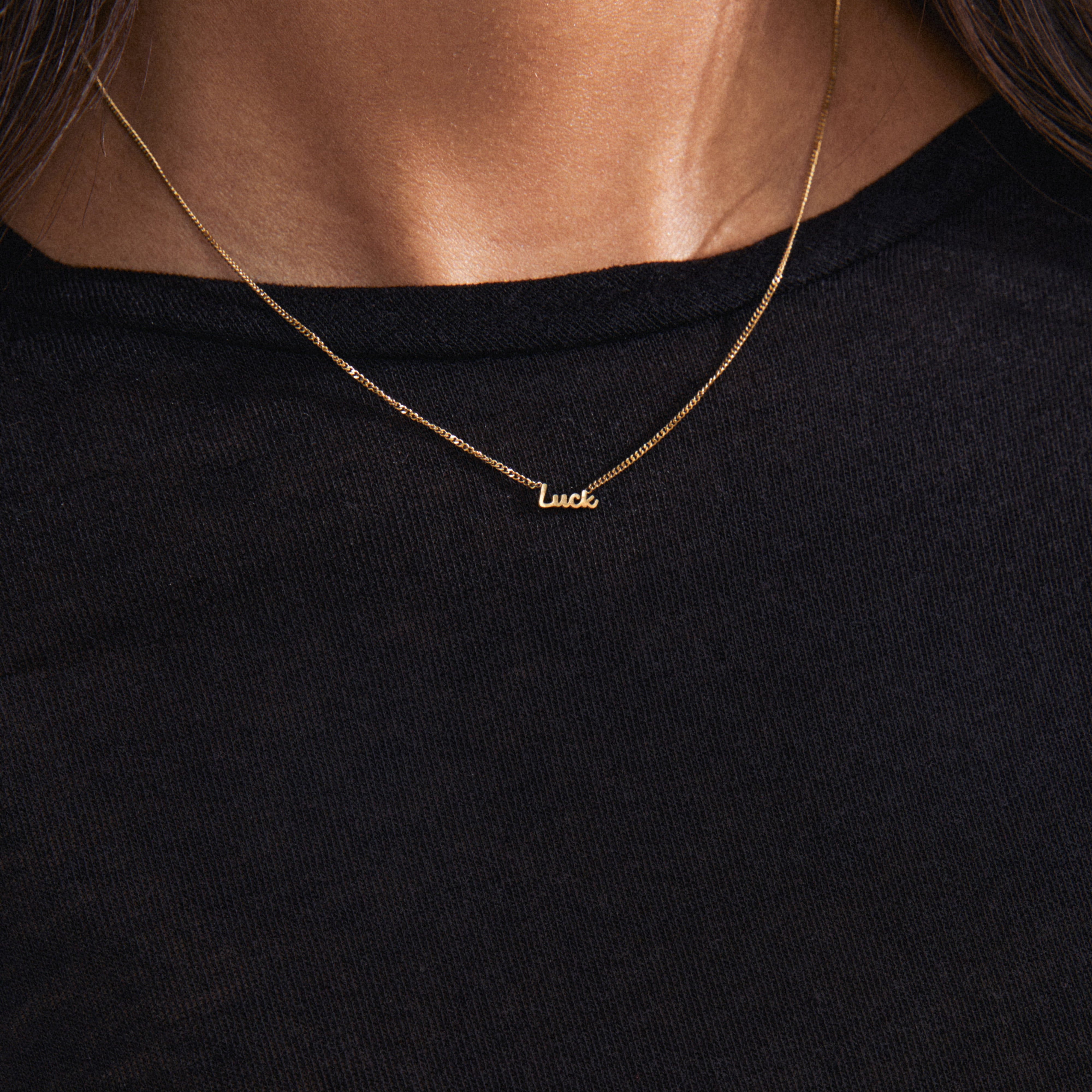Gold-plated LUCK necklace with a cursive script pendant, worn by a person. A versatile, genderless accessory perfect for layering and personal styling.