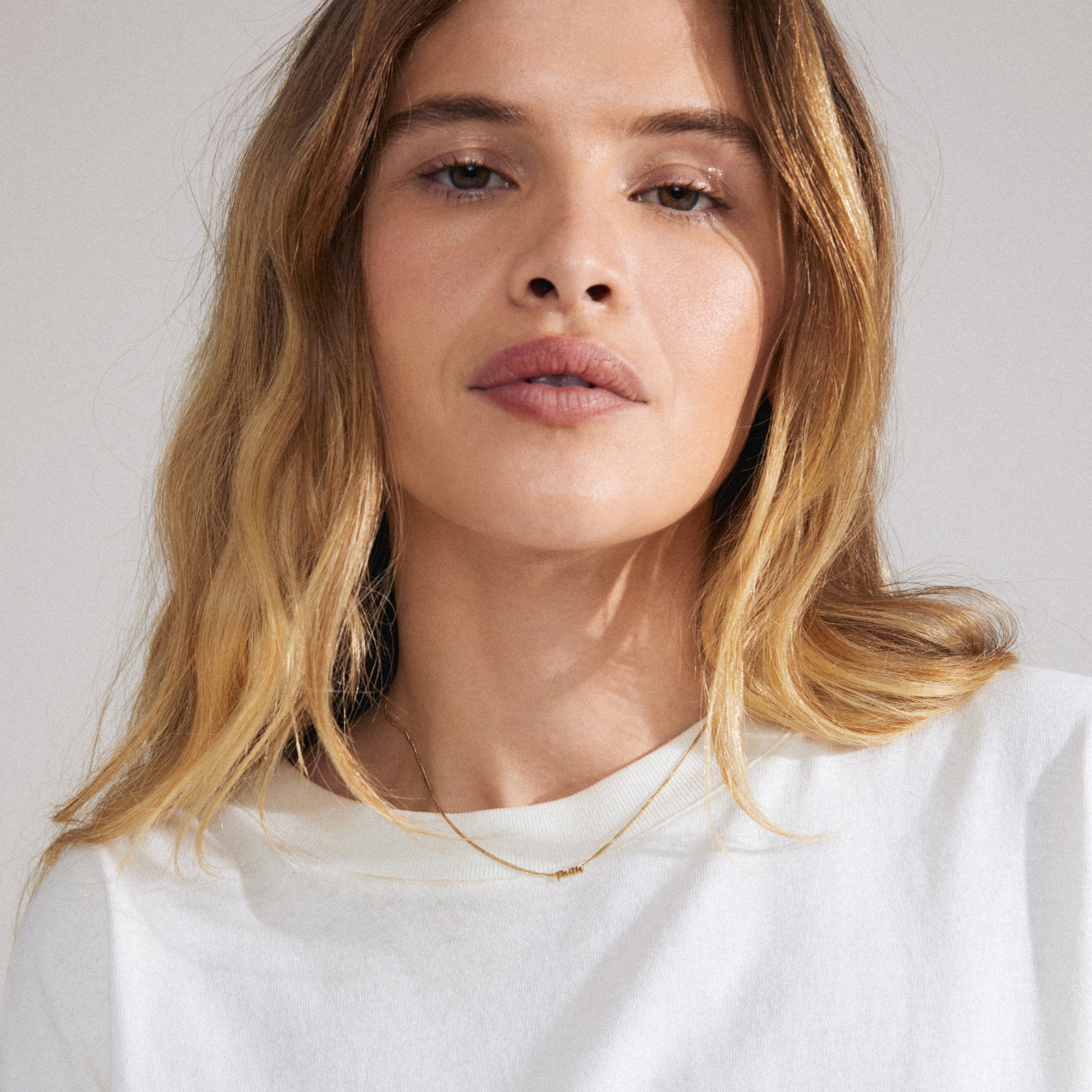 Gold-plated FAITH necklace on a woman, featuring a cursive script pendant, embodying a sleek, genderless design ideal for layering and personal expression.
