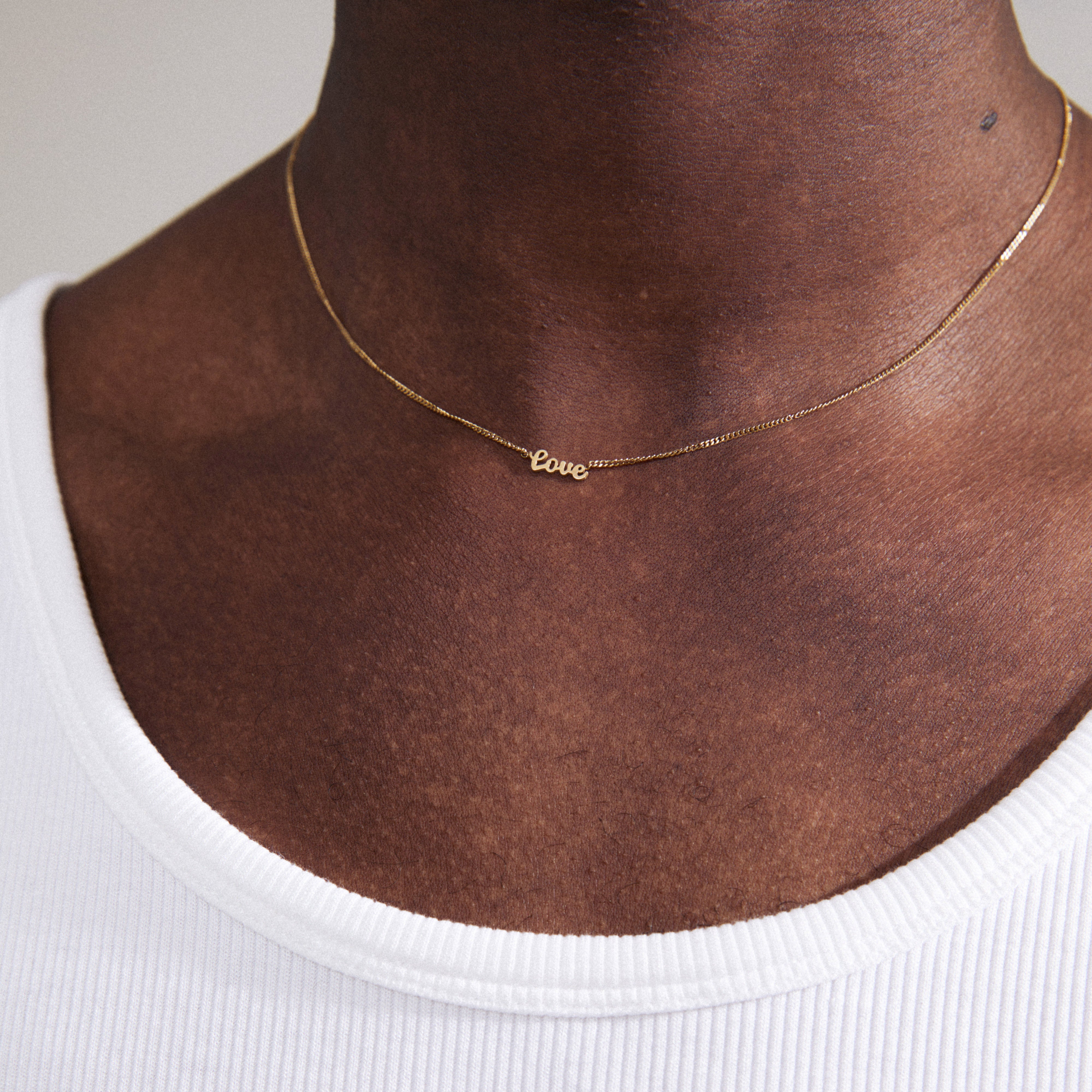 Gold-plated LOVE necklace with cursive script pendant, worn by a person. A sleek, genderless fashion accessory, perfect for layering or solo wear.