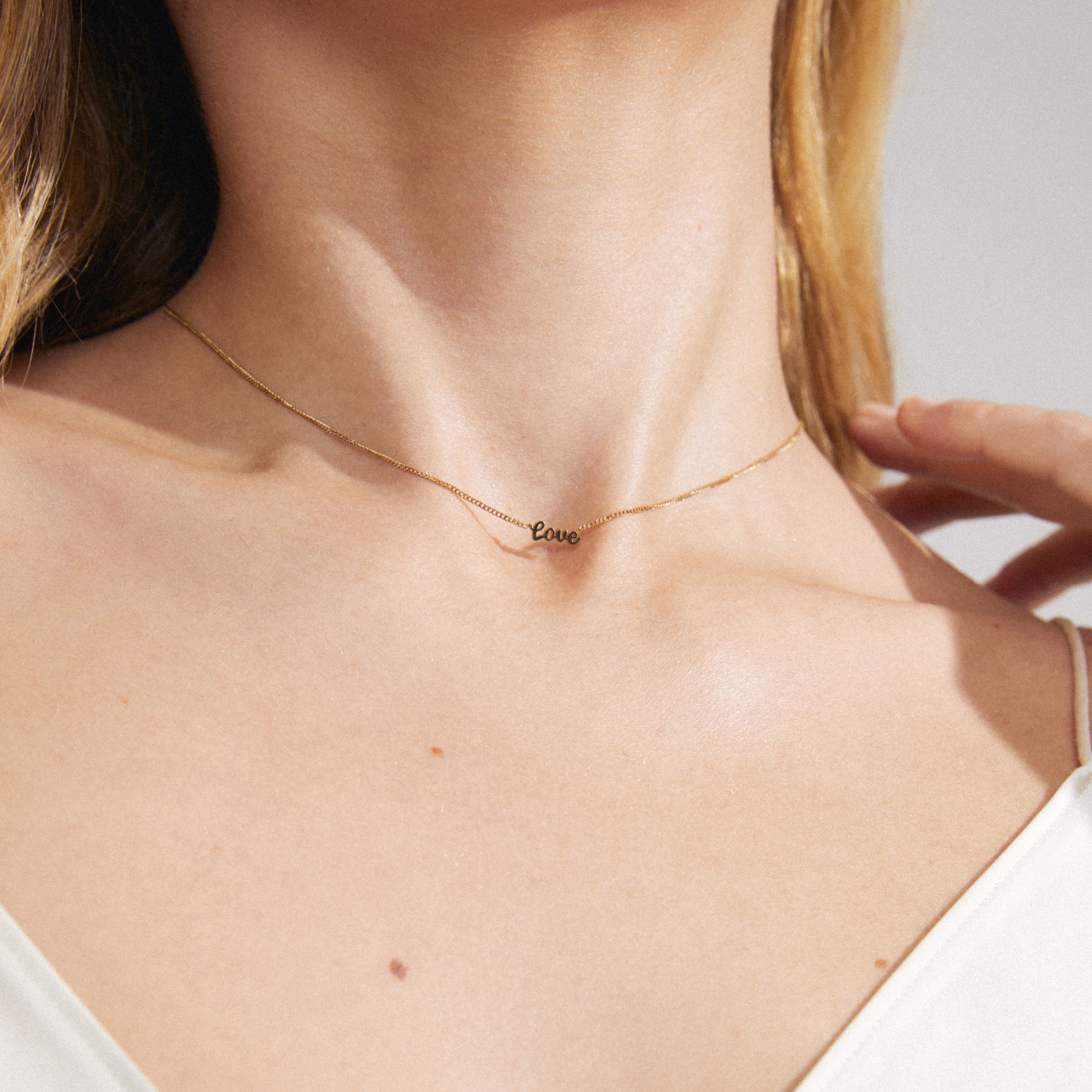Gold-plated LOVE necklace with cursive pendant on a woman's neck, showcasing a genderless design perfect for layering and everyday wear.