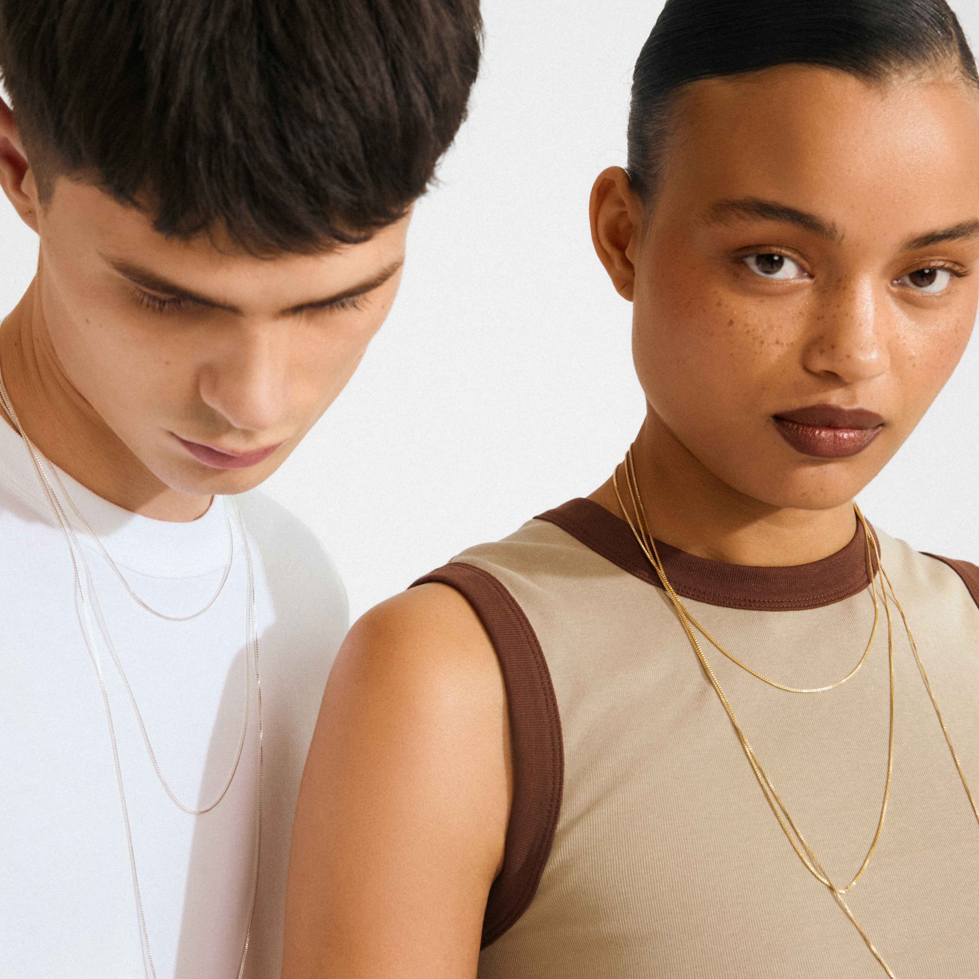 Two young adults showcase layered necklaces using the gold-plated Lock with 3 lobsters clasp, elegantly preventing tangling for a trendy, editorial look.