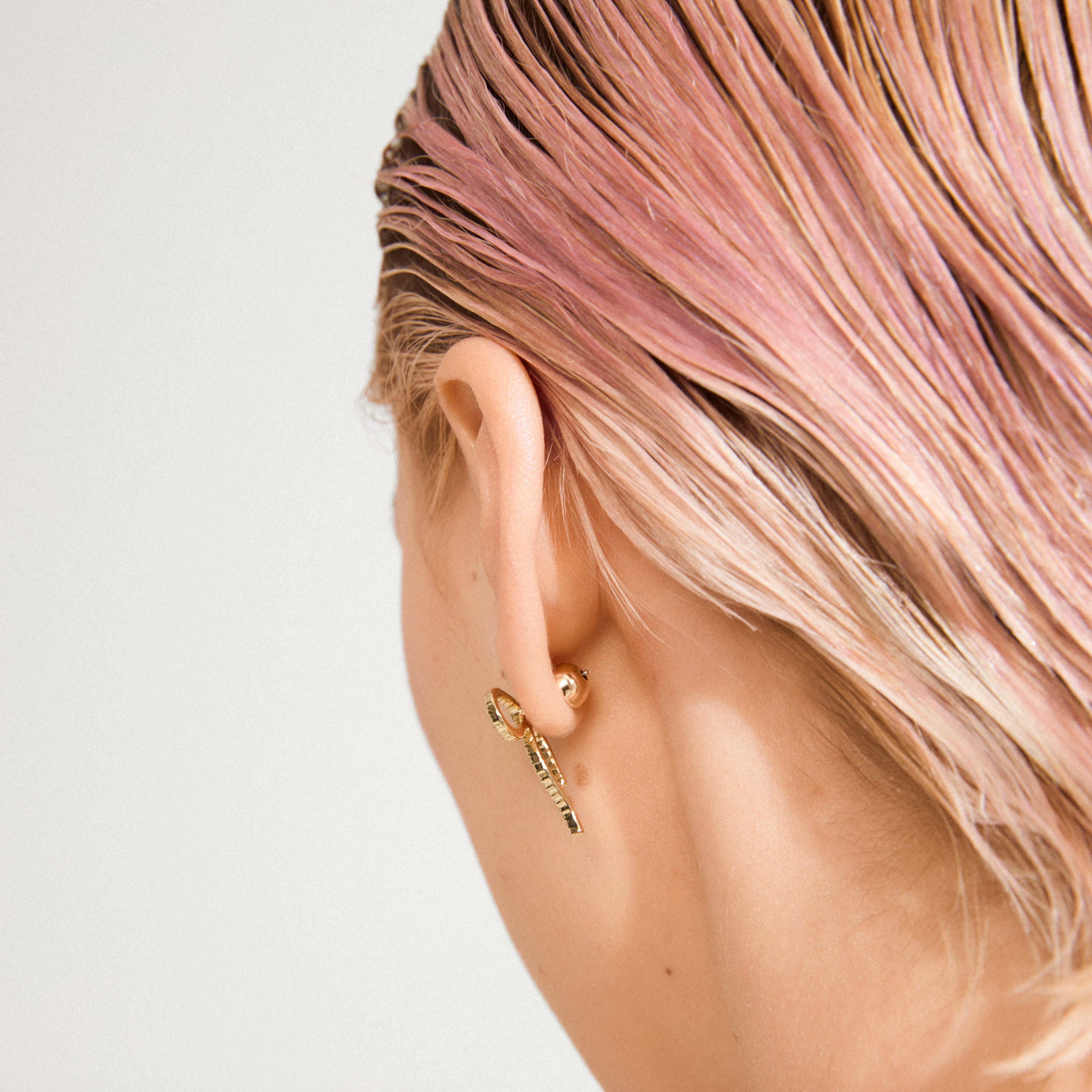 Close-up of an ear wearing a gold-plated stud with a decorative bullet lock bead, 7 mm, and a dangling bar earring.