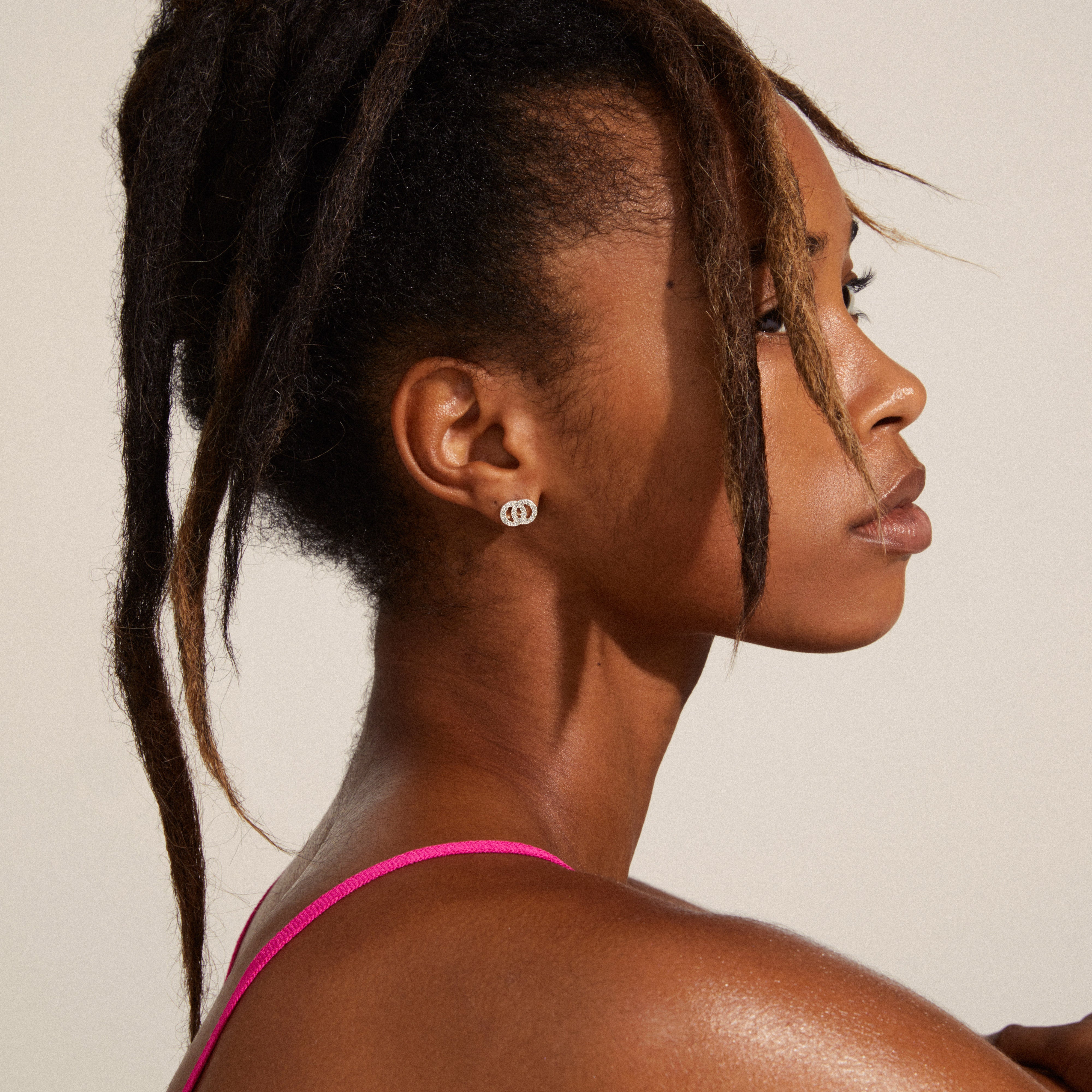 Woman wearing VICTORIA crystal earrings, silver-plated, featuring intertwined rings with bright crystal stones, highlighting a contemporary, fashionable style.