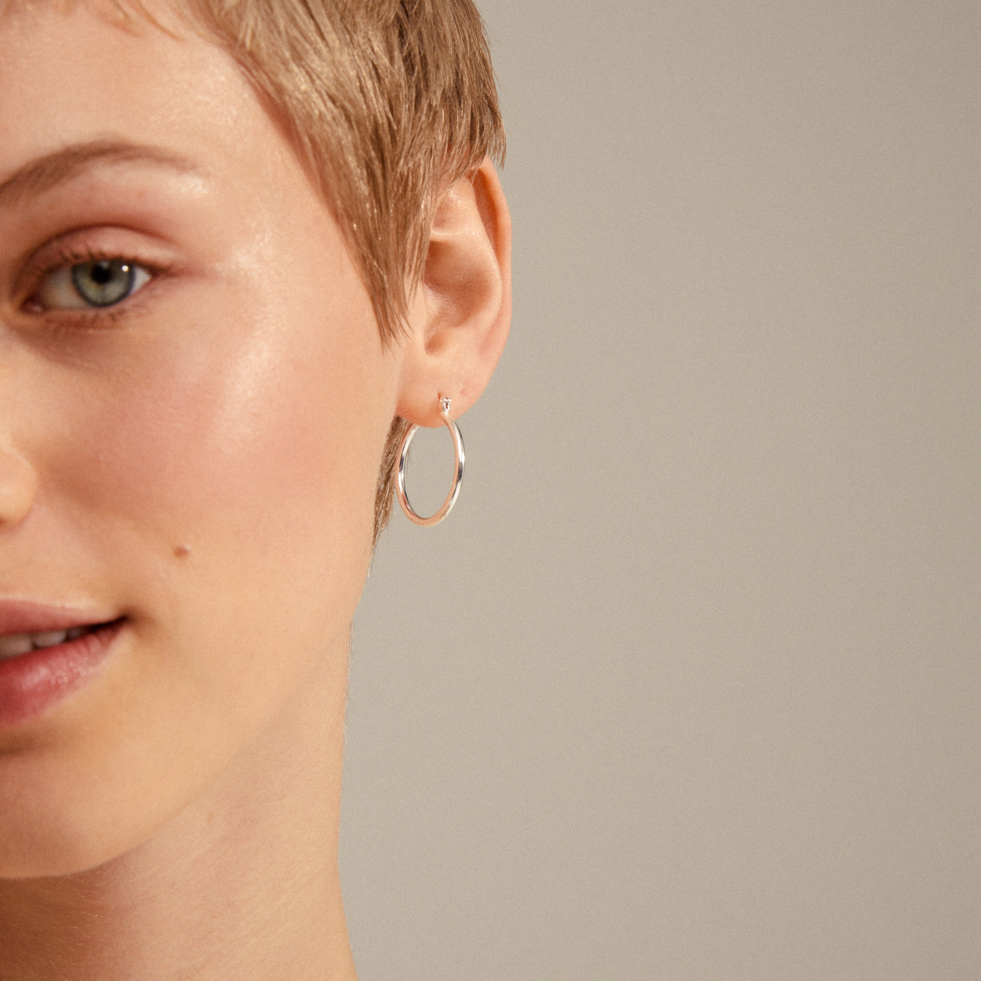LAYLA medium hoop earrings, silver-plated, adorn a woman's ear, highlighting their elegant, timeless design and easy click clasp. Perfect for any stylish ensemble.