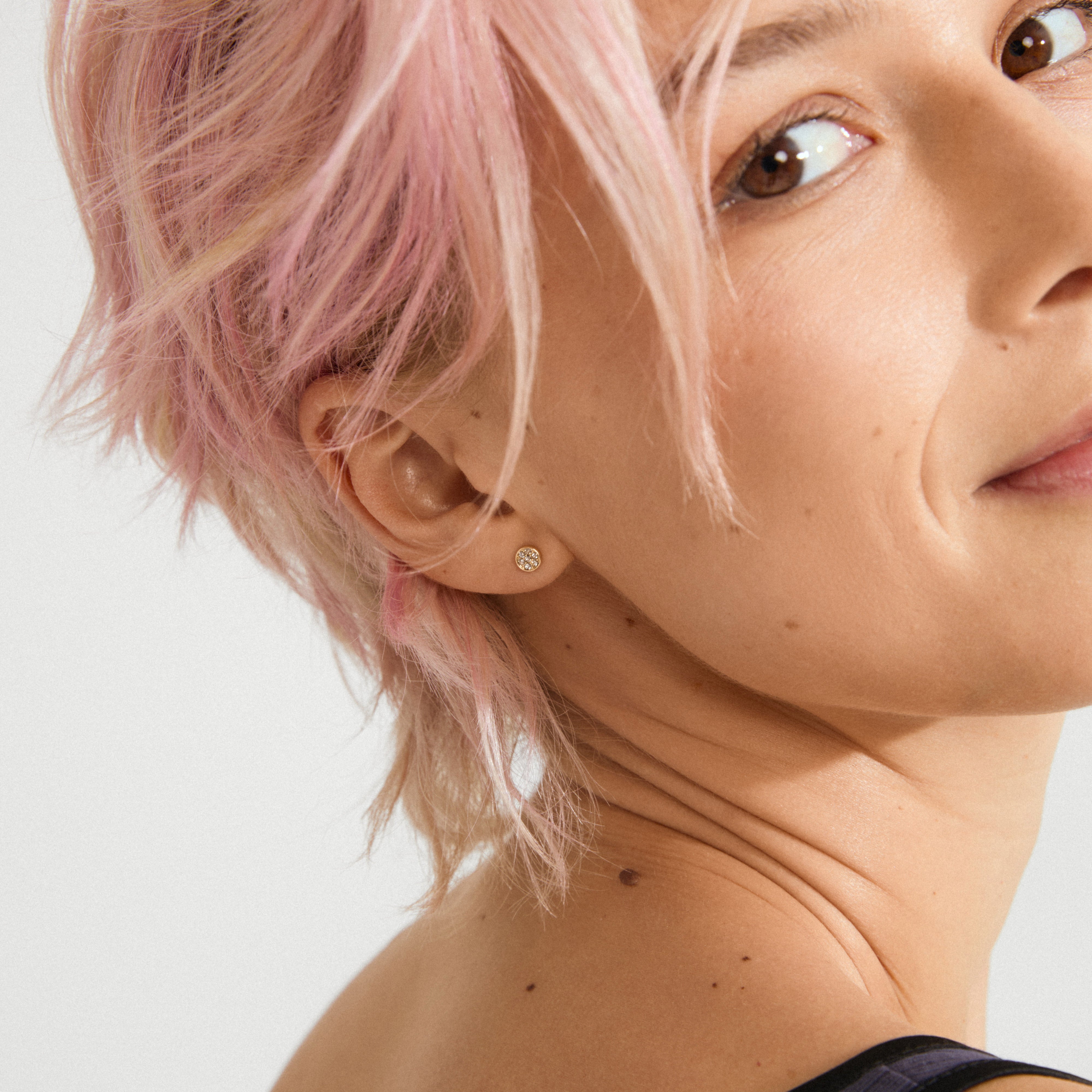 Side profile showcasing EMMA crystal earrings gold-plated; small round studs with sparkling crystals, highlighting elegance and simplicity against a light background.