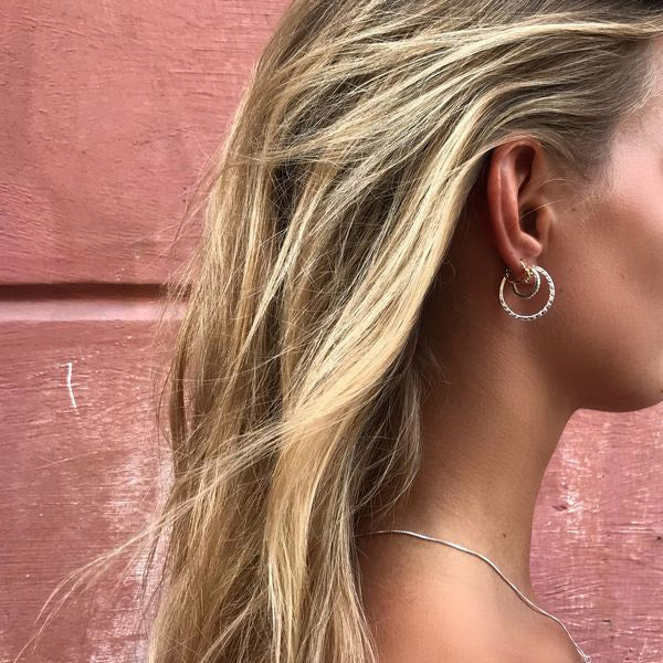 Profile of a woman wearing ROBERTA small crystal semi-hoops, gold-plated, showcasing the earrings' Nordic simplicity and clear crystal elegance.