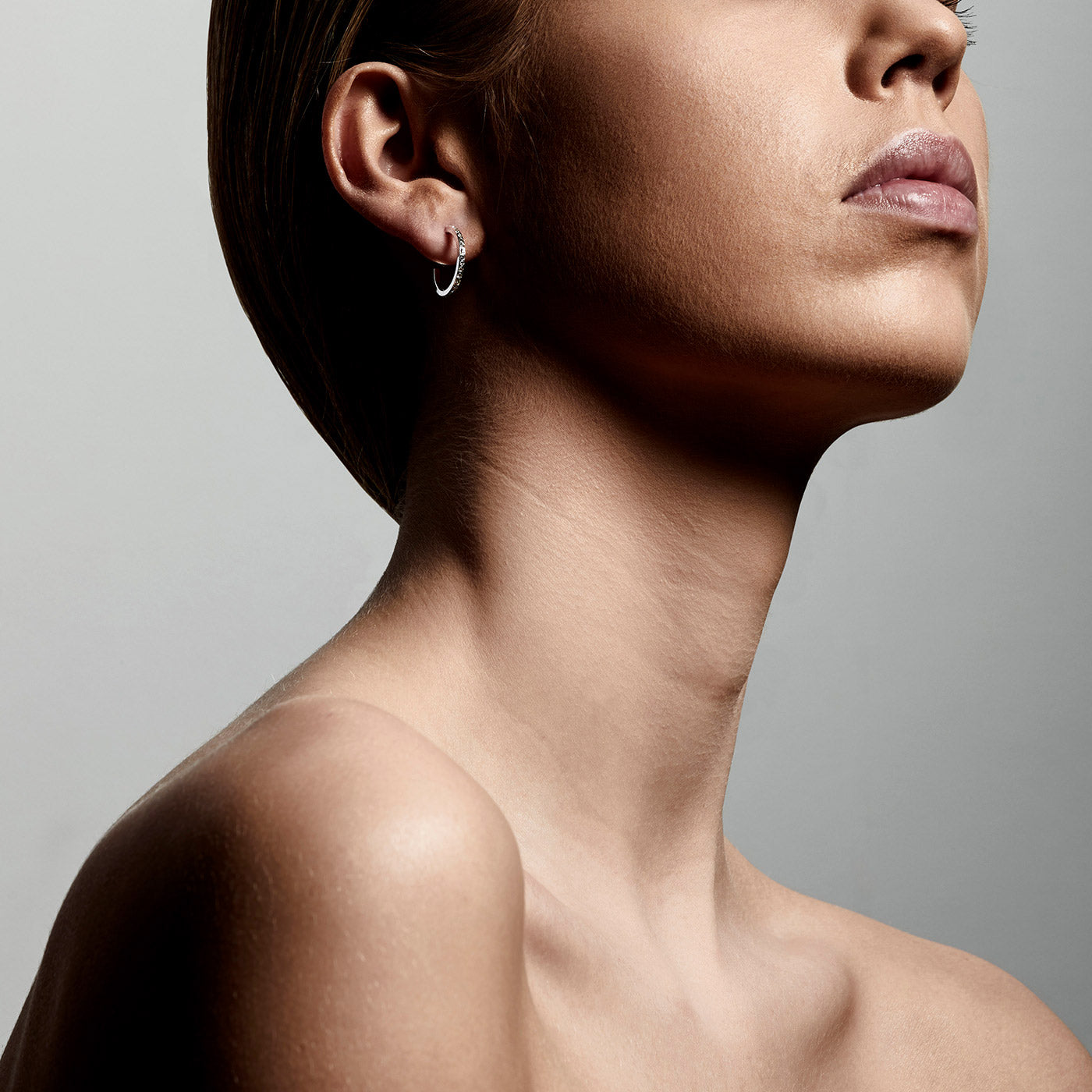A close-up of a woman's ear wearing ROBERTA crystal semi-hoops, silver-plated, showcasing the hoop's elegant, Nordic-inspired simplicity and crystal embellishments.