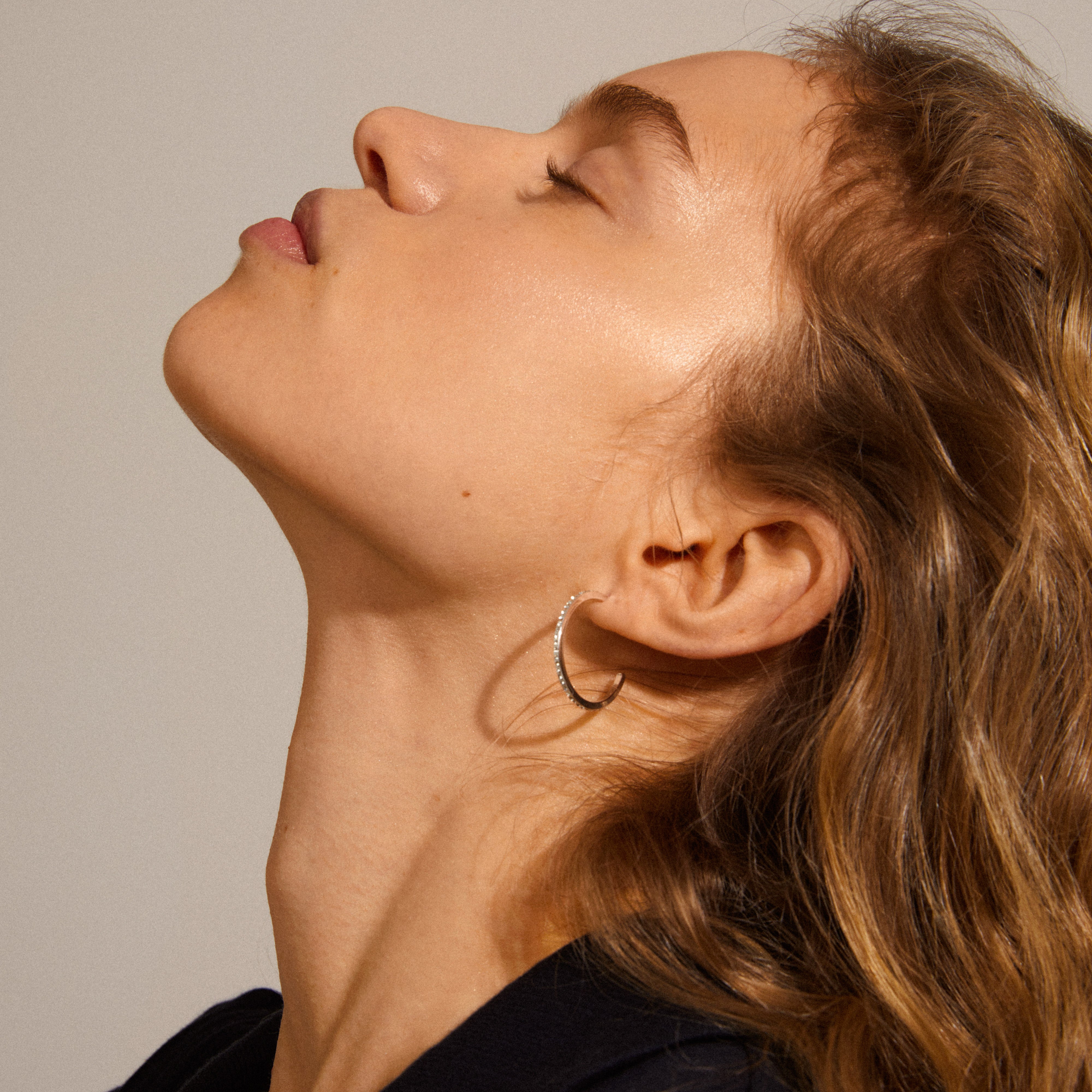 Roberta large crystal semi-hoops, silver-plated, worn by a woman with closed eyes, showcasing their brilliant, classic Nordic design and sparkling crystals.